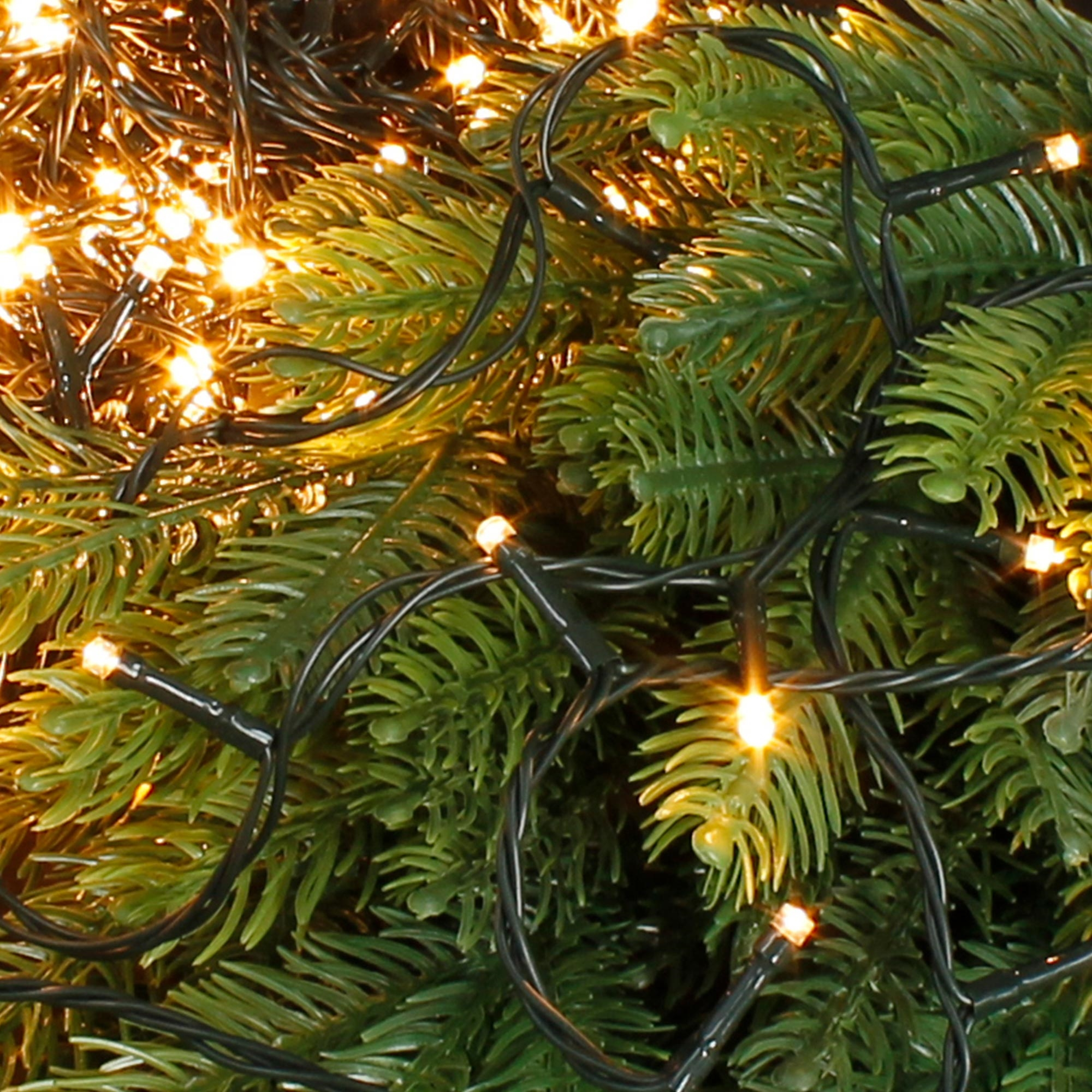 Nahaufnahme eines Weihnachtsbaums mit grünen Nadeln und kleinen, warmweißen LED-Lichtern zwischen den Zweigen.