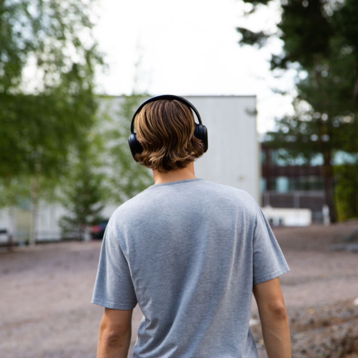 Osoba w słuchawkach odchodzi od kamery. Ma na sobie szarą koszulkę, a w tle widać budynki i drzewa.