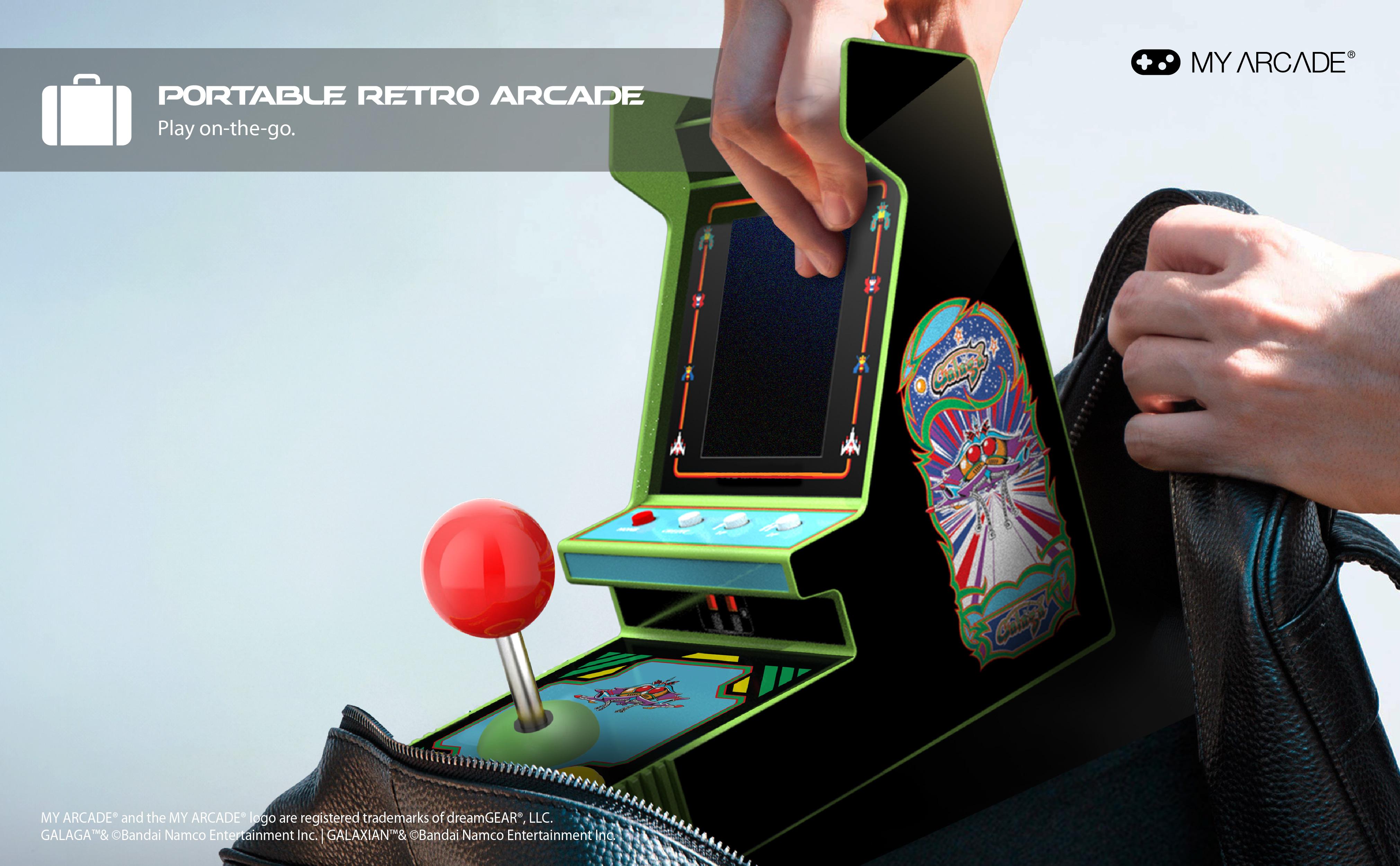 Una persona tiene un cabinato arcade retrò portatile, joystick rosso, dettagli verdi, sfondo nero, tirato fuori da una borsa.