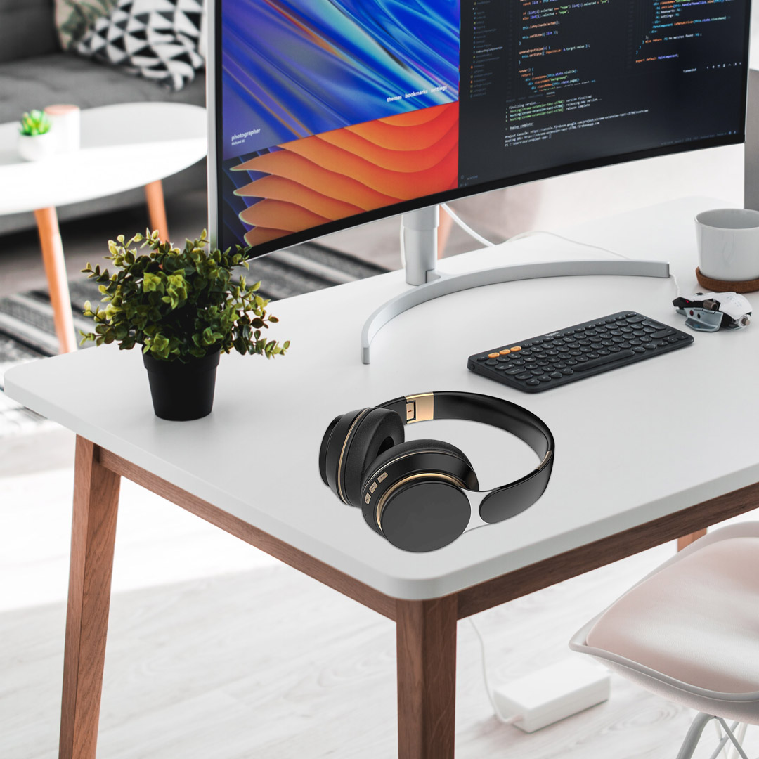 Biurko ze słuchawkami, klawiaturą, monitorem i rośliną. Monitor wyświetla kod i kolorową sztukę abstrakcyjną. Czarne i złote słuchawki.