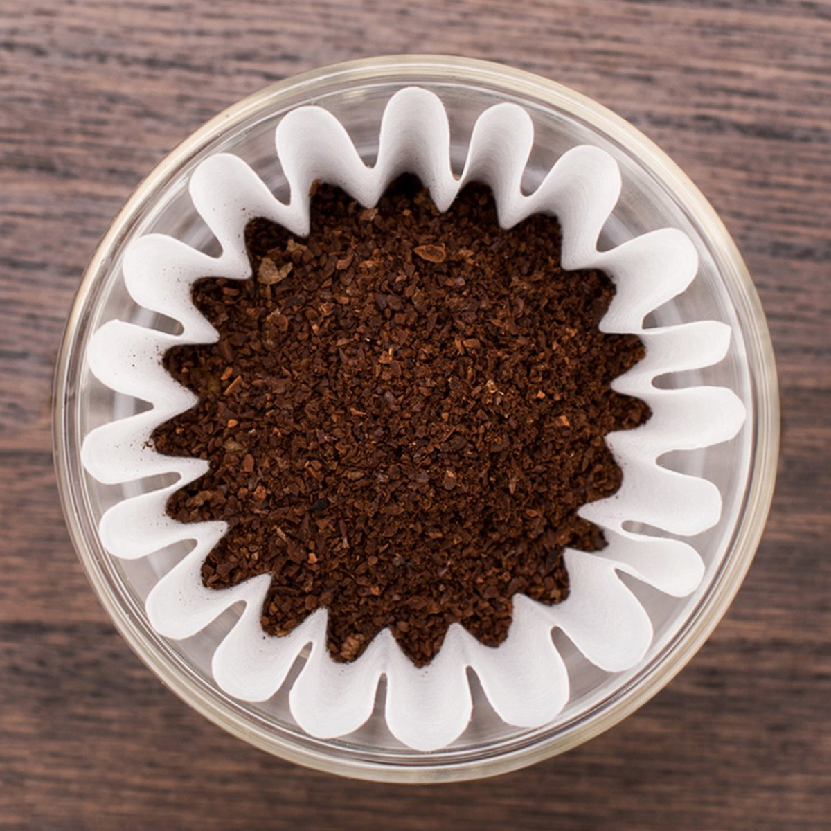 Draufsicht auf ein Glas mit einem weißen Papier-Kaffeefilter, gefüllt mit braunem Kaffeesatz, auf Holzoberfläche.