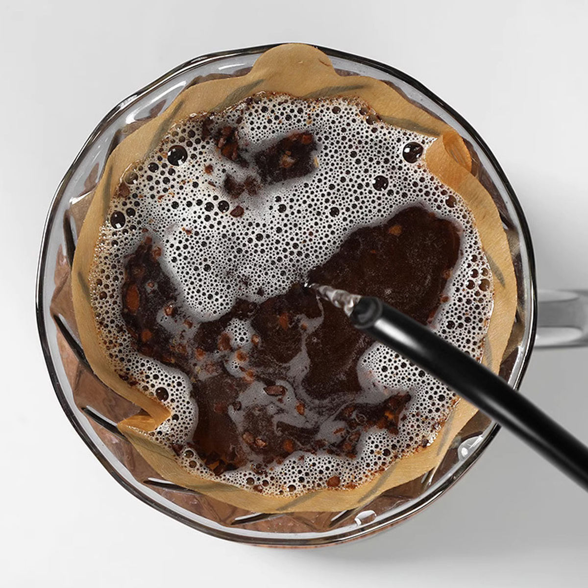 Draufsicht auf Kaffeezubereitung. Brauner Filter, dunkler Kaffee, Blasen und ein schwarzer Pour-Over-Ausguss sind sichtbar.