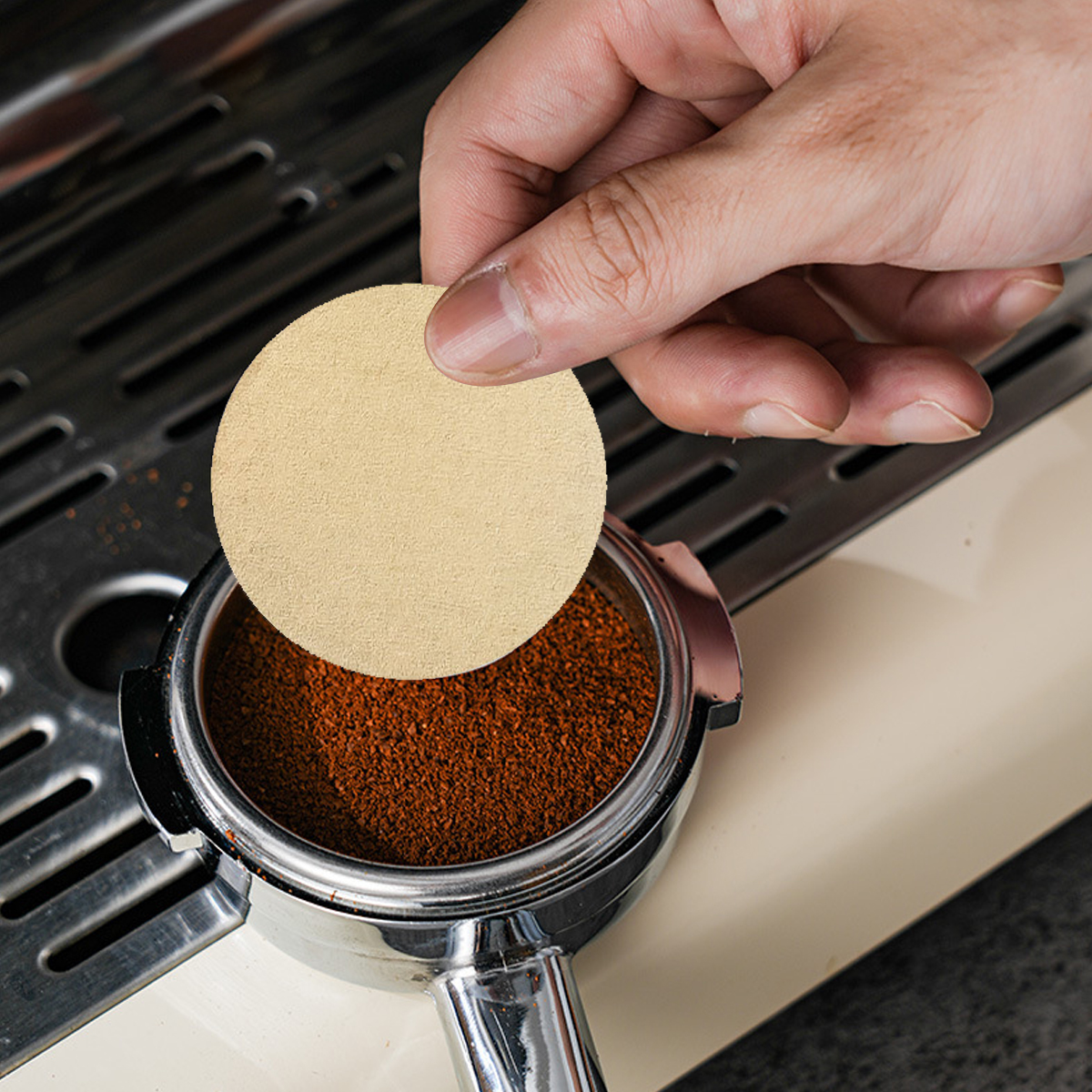 Eine Hand legt Filterpapier auf gemahlenen Kaffee in einem Siebträger. Der Hintergrund zeigt Teile der Maschine.