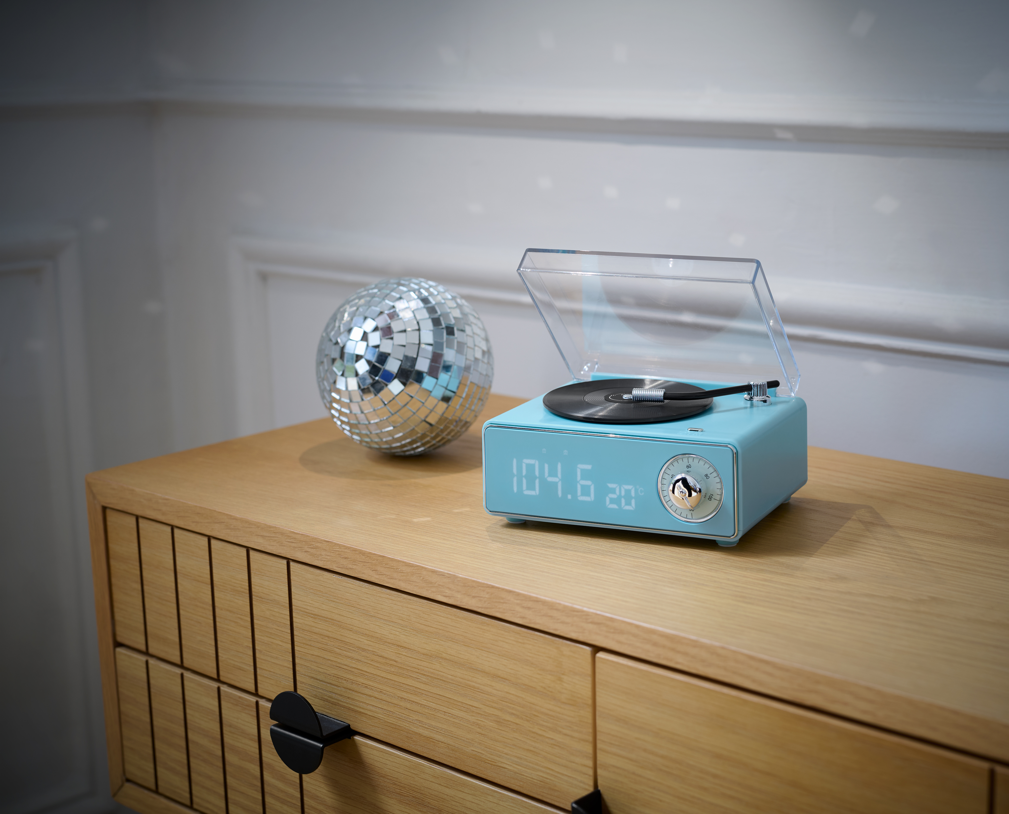 Une platine vinyle bleue avec un disque dessus, une boule disco et un meuble en bois. Le fond est blanc.