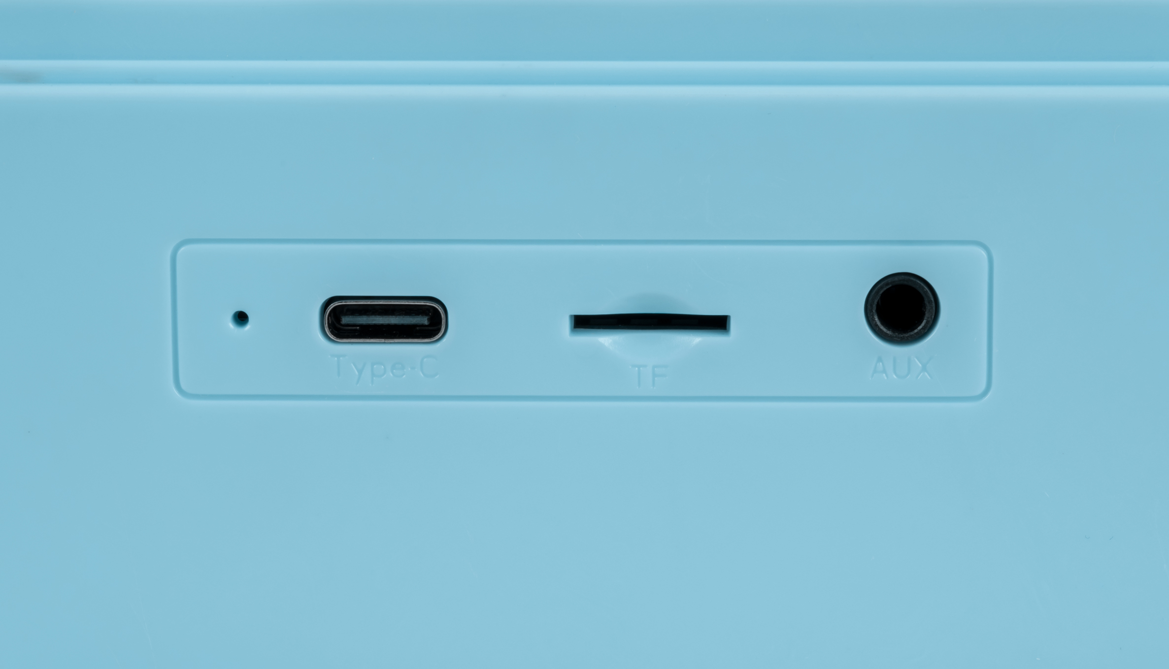 Gros plan d'un appareil bleu clair avec des ports Type-C, TF et AUX. Un petit point est également visible.