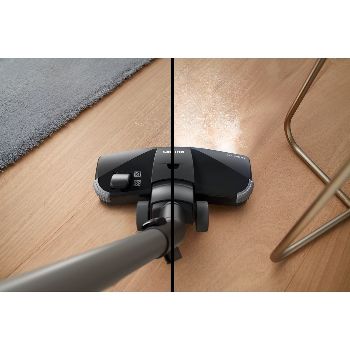 Odkurzacz Philips na drewnianej podłodze. Kurz jest zasysany z jednej strony. Widoczny jest również szary dywan i złota noga krzesła.