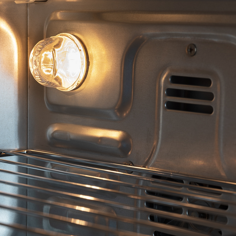 All'interno di un forno. Una lampadina accesa è a sinistra. Griglia e interno metallici visibili. Il forno è pulito.