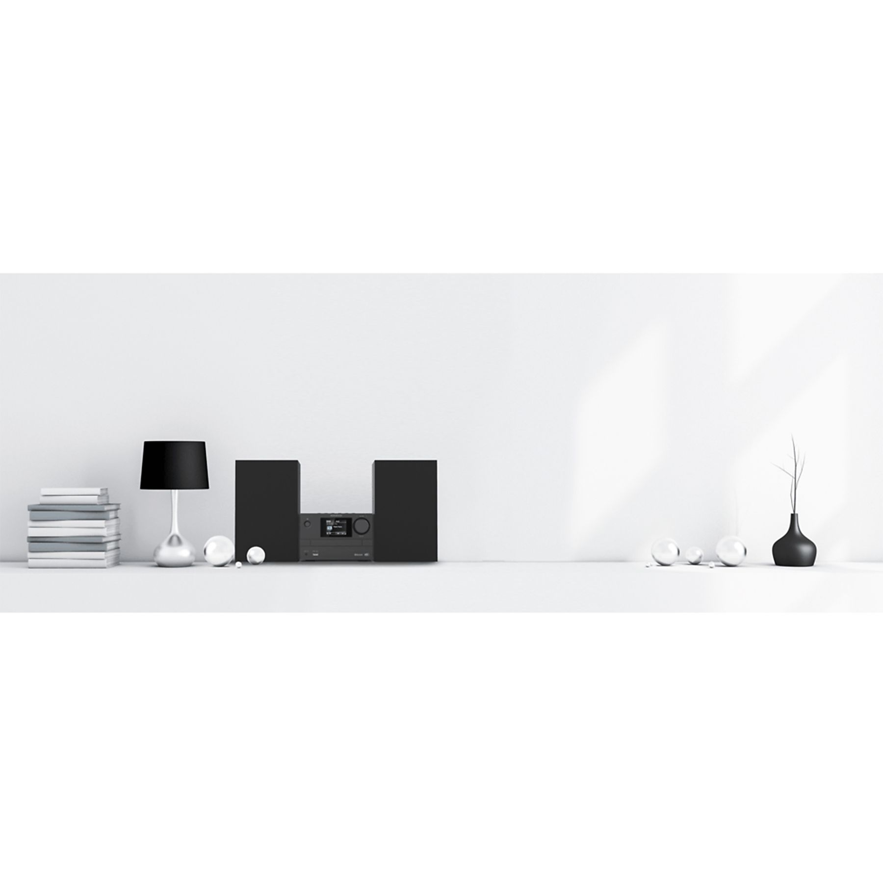 Una configuración minimalista con altavoces negros, una lámpara y decoración sobre una superficie blanca. El fondo es blanco.