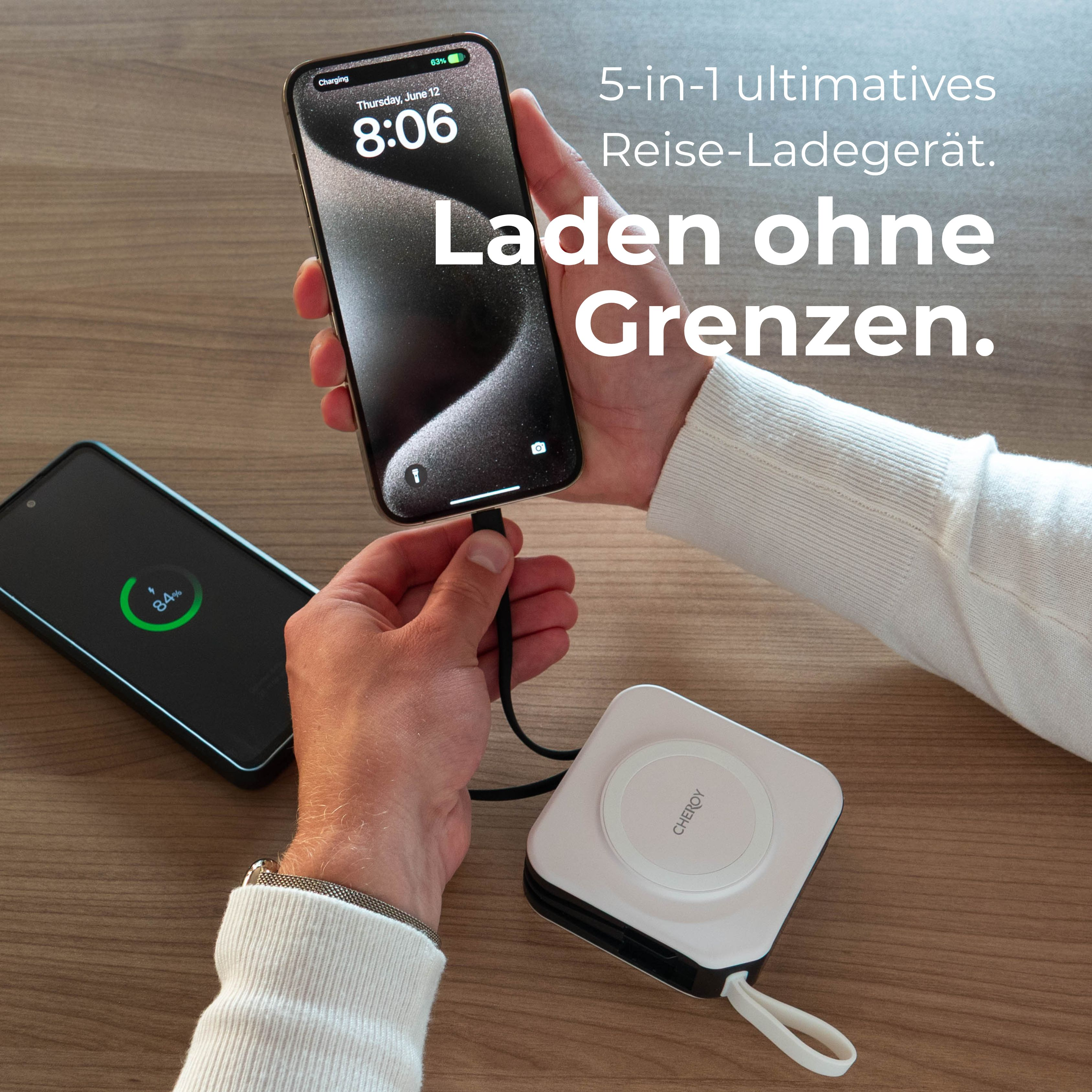 Eine Person, die ein Telefon mit einem Kabel auflädt. Ein anderes Telefon und ein Ladegerät auf Holz.