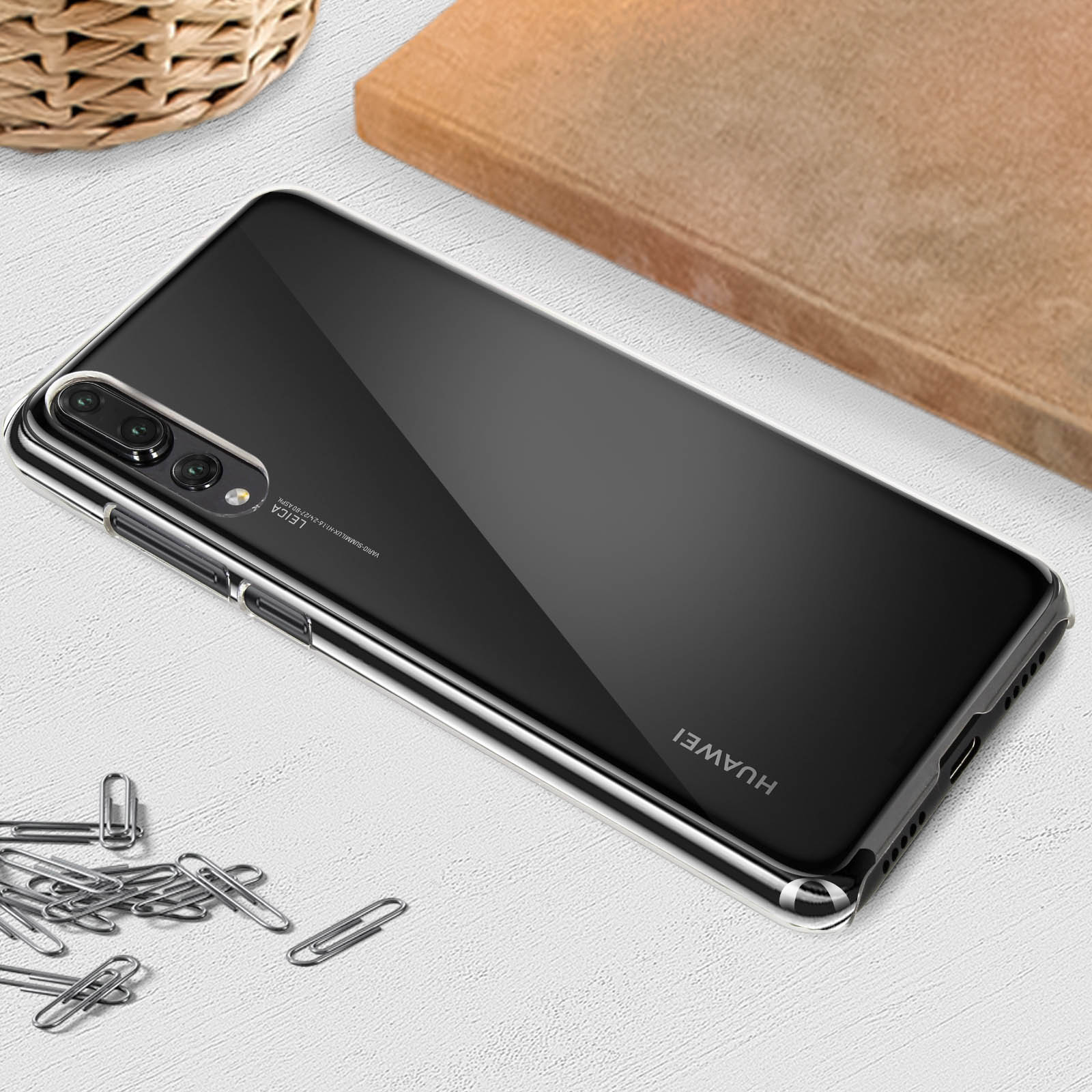 Telefono Huawei nero con custodia trasparente su superficie bianca. Graffette e blocco di legno nelle vicinanze.