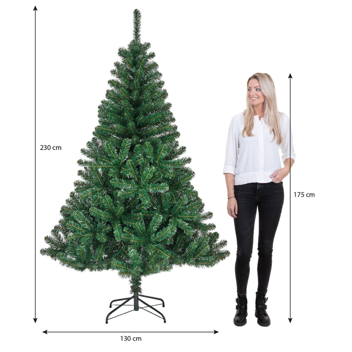 Un sapin de Noël artificiel vert se trouve à côté d'une femme. Mesures: arbre 230 cm de haut, 130 cm de large; femme 175 cm de haut.