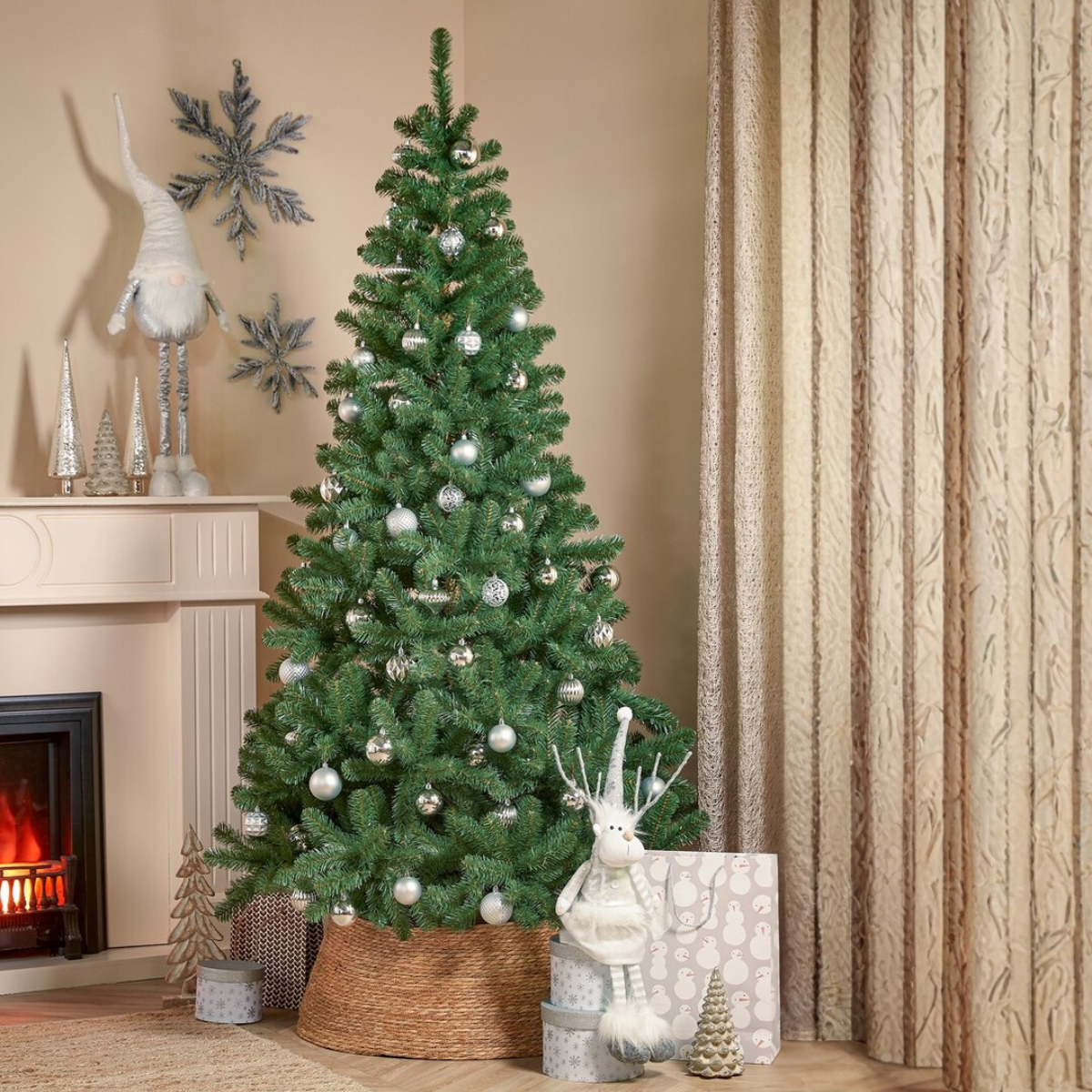 Un sapin de Noël décoré d'ornements argentés se dresse dans une pièce. Une cheminée, des décorations et un rideau sont également visibles.