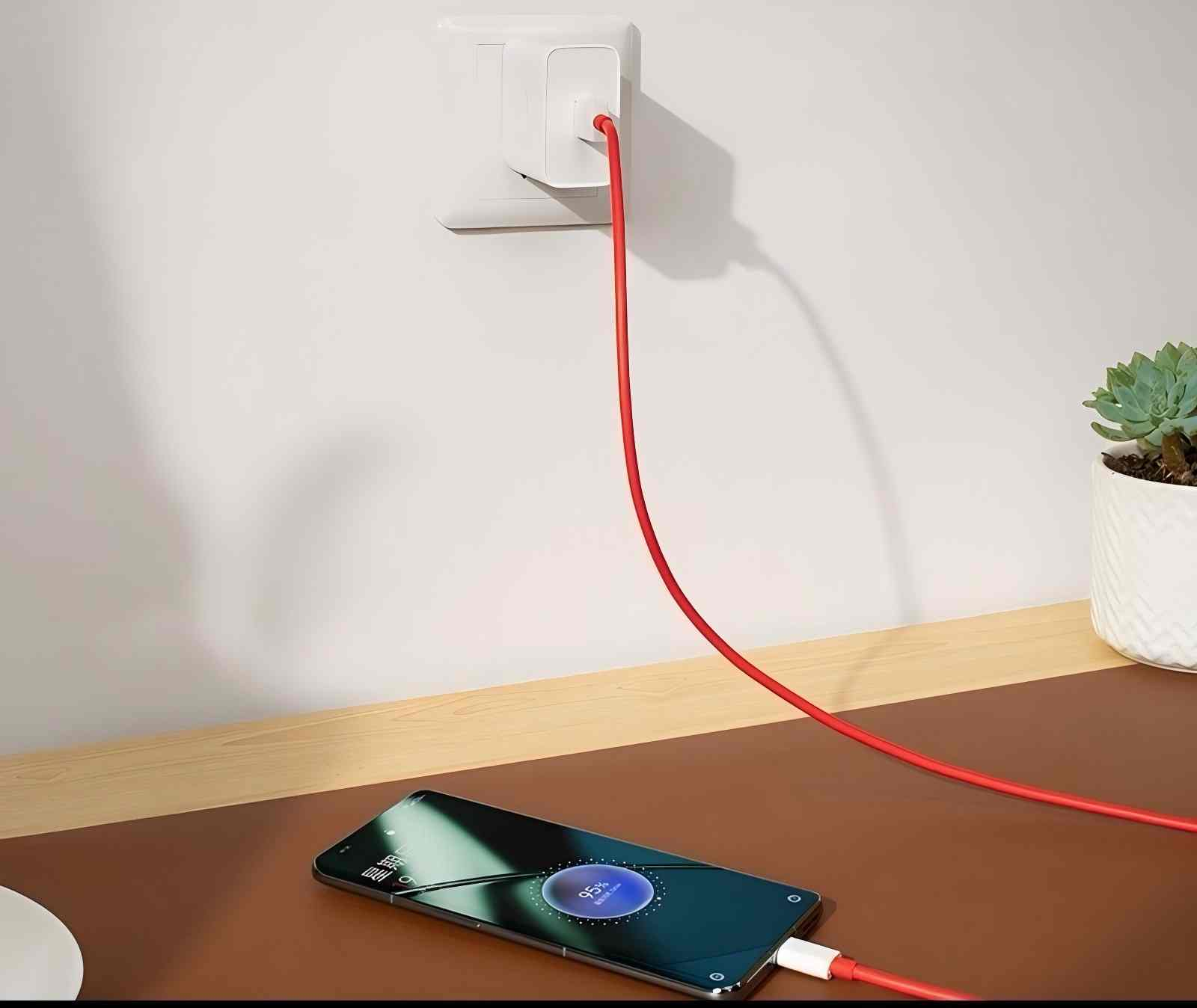 Un teléfono cargándose sobre una superficie marrón con un cable rojo conectado a un cargador de pared blanco.