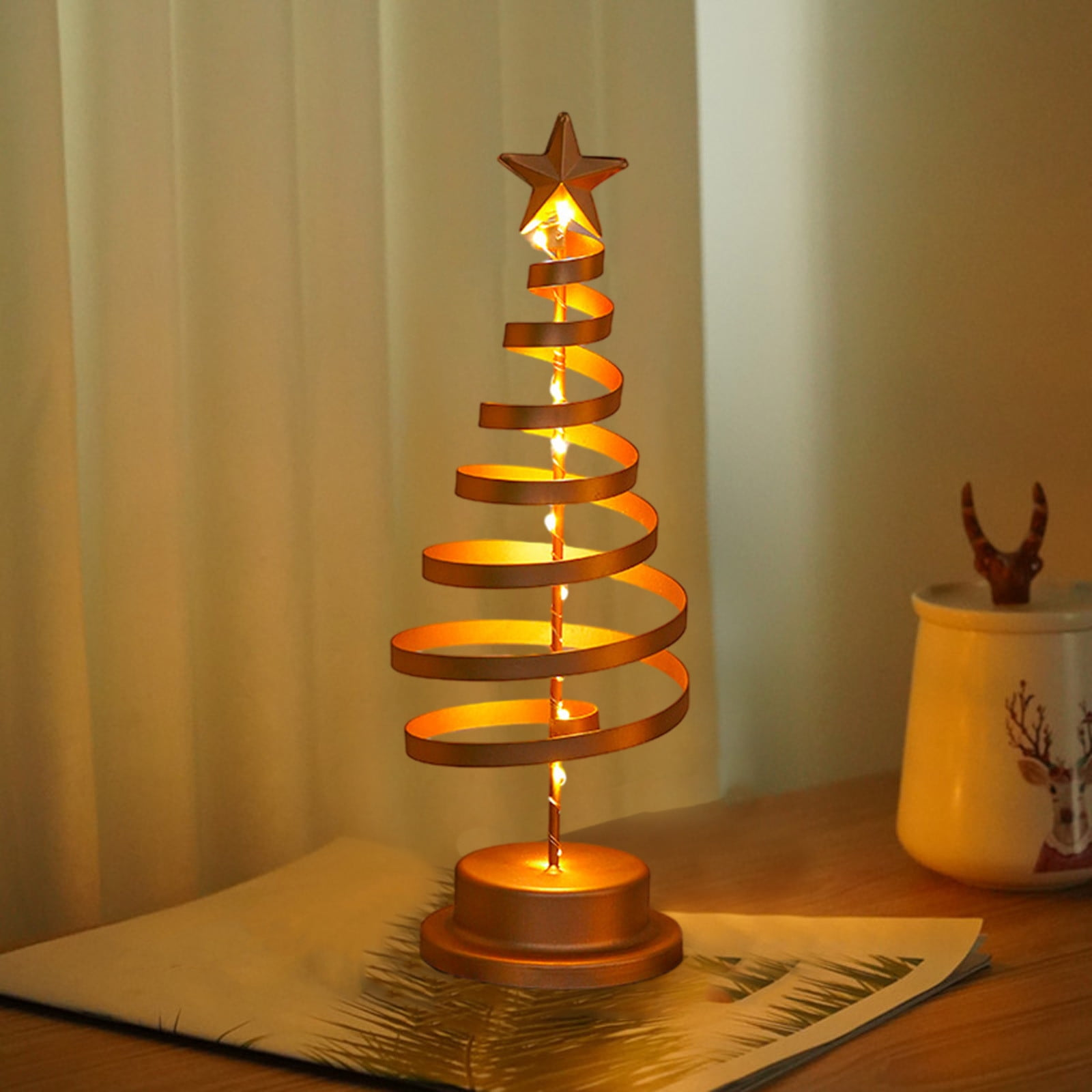 Goldener Weihnachtsbaum in Spiralform mit Stern. Beleuchtet mit kleinen Lichtern, auf einem Tisch neben einem Glas.