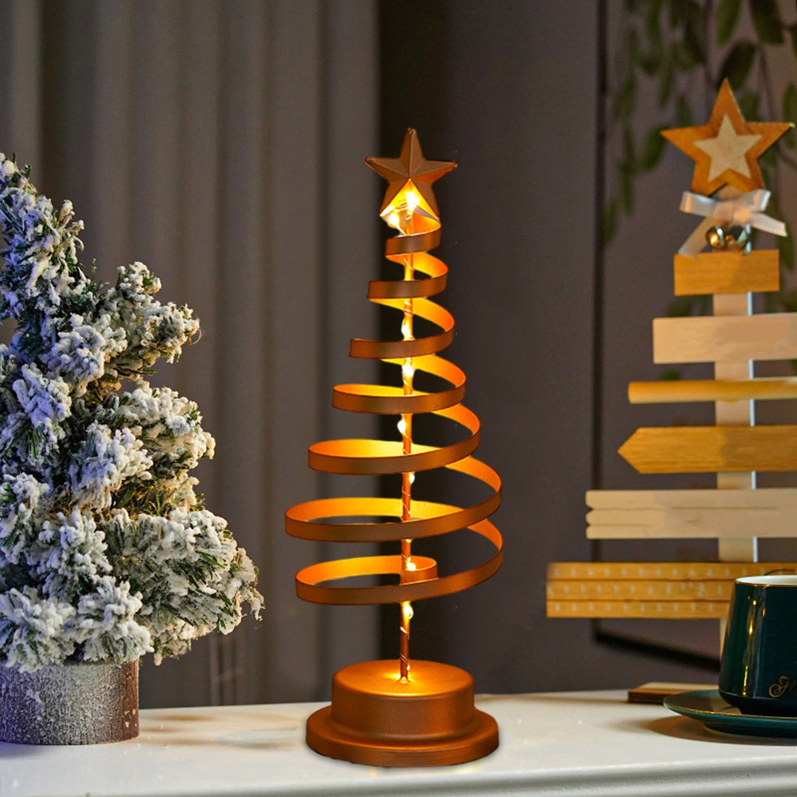 Ein dekorativer Weihnachtsbaum aus Metallspulen. Obenauf sitzt ein Stern. Links ist ein verschneiter Baum.