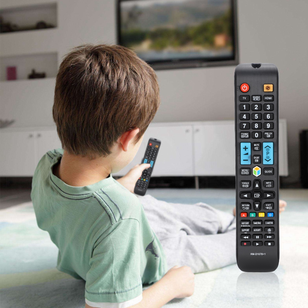 Ein Kind hält eine Fernbedienung und schaut auf einen Fernseher. Eine größere Fernbedienung ist im Vordergrund. Ein weißer Schrank ist im Hintergrund.