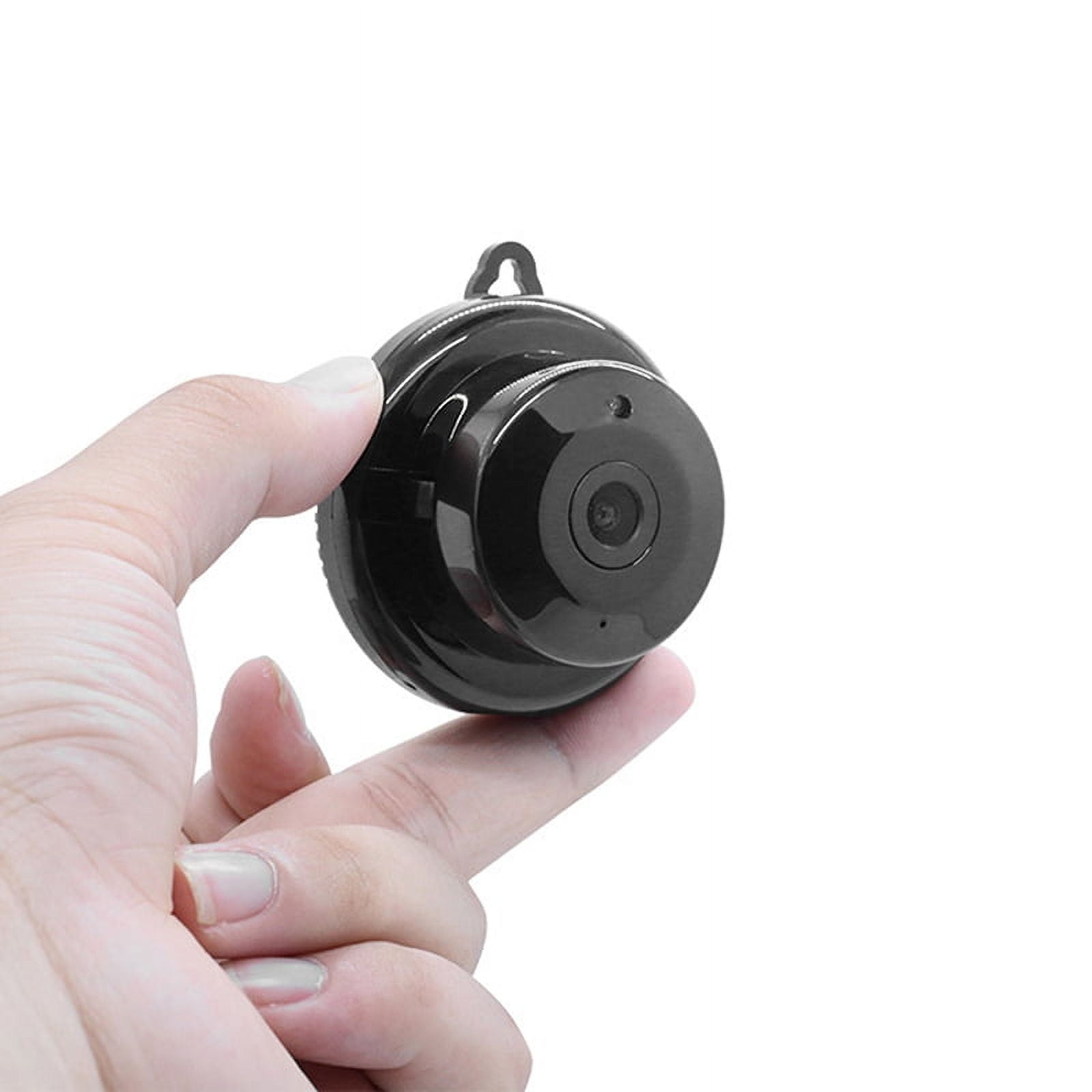 Eine Hand, die eine kleine, schwarze, runde Überwachungskamera mit Linse auf weißem Hintergrund hält.