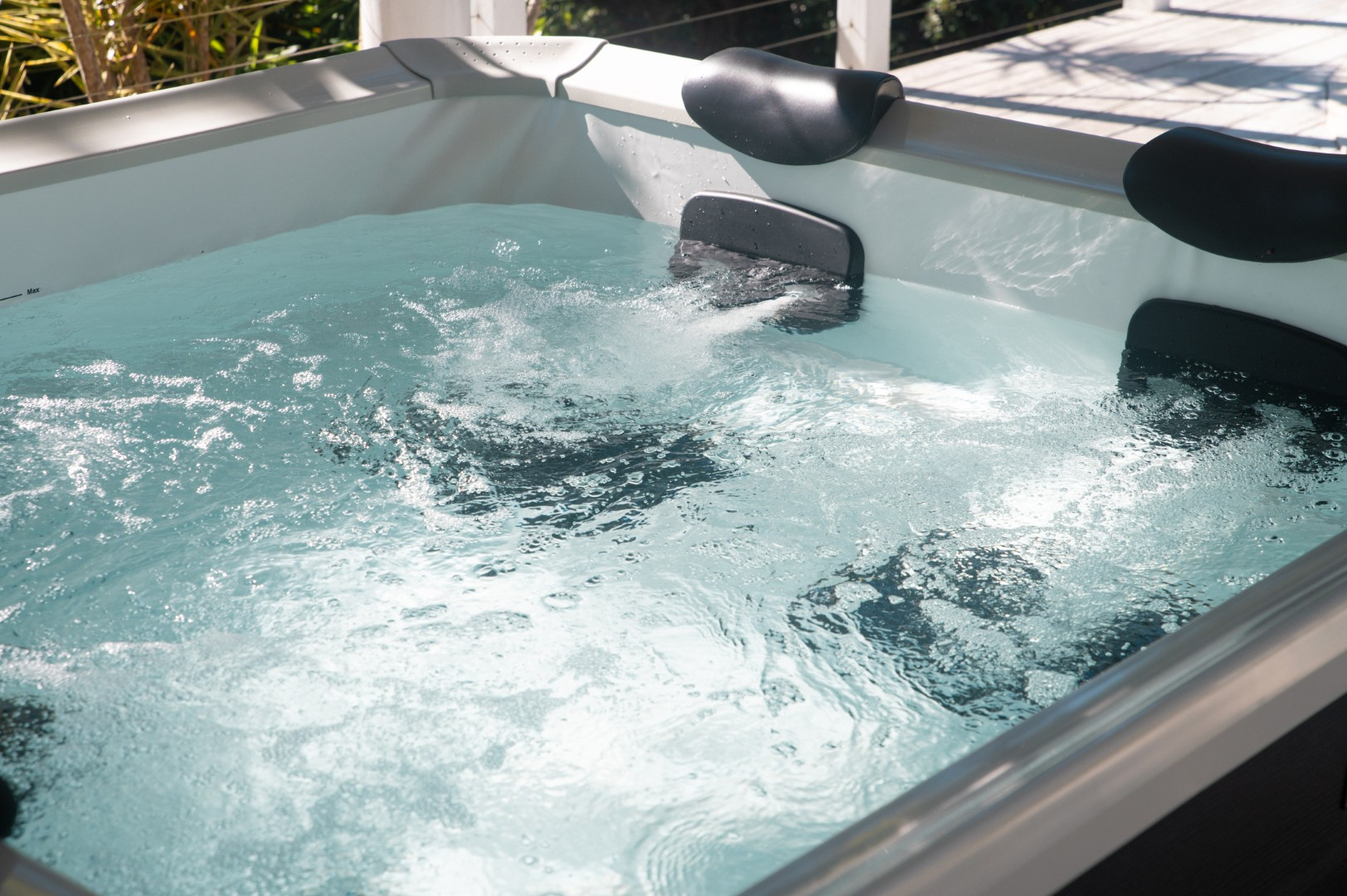 Nahaufnahme eines Whirlpools mit klarem, sprudelndem Wasser. Schwarze Kopfstützen sind sichtbar, der Whirlpool steht auf einem Holzdeck.