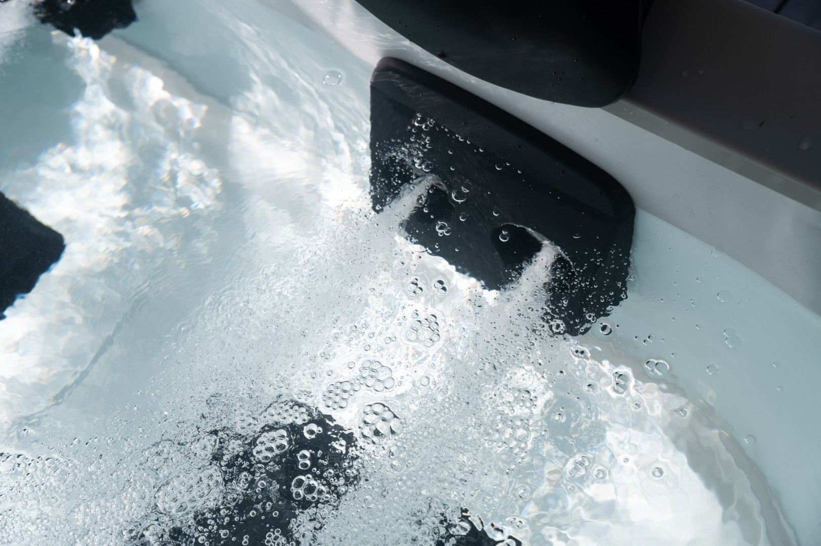 Nahaufnahme eines Whirlpools. Blasen steigen in klarem Wasser auf, das aus einer schwarzen Düse strömt. Der Rand des Whirlpools ist sichtbar.