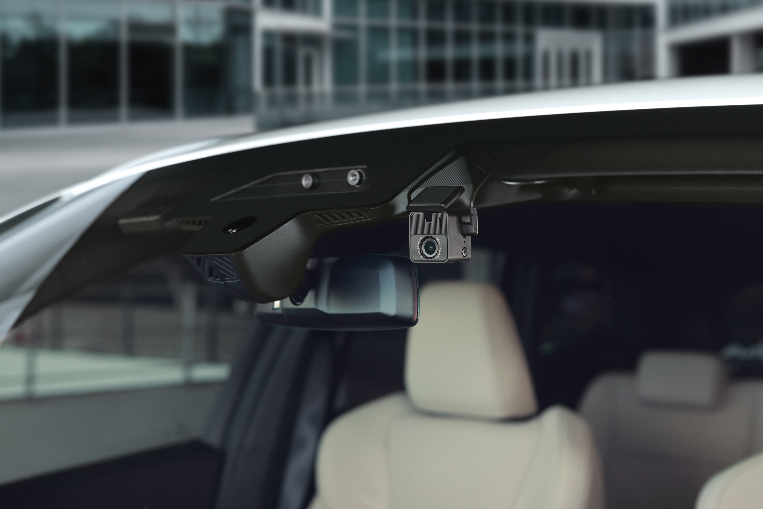 Autointerieur mit Dashcam, Rückspiegel und cremefarbenen Sitzen. Gebäudeaußenansicht durch die Windschutzscheibe sichtbar.