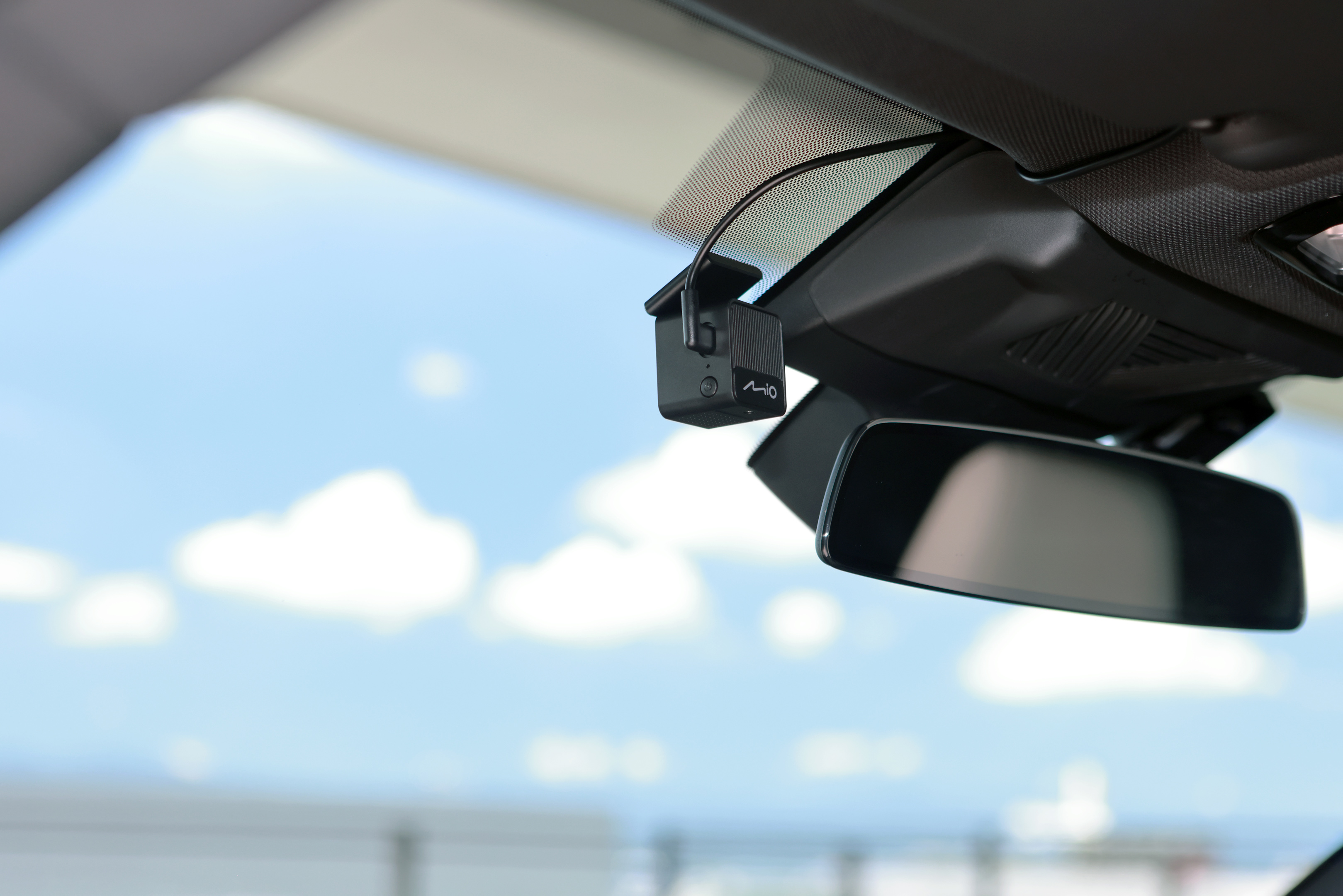 Autoinnenraum. Eine Dashcam und ein Rückspiegel sind vor blauem Himmel mit Wolken zu sehen.