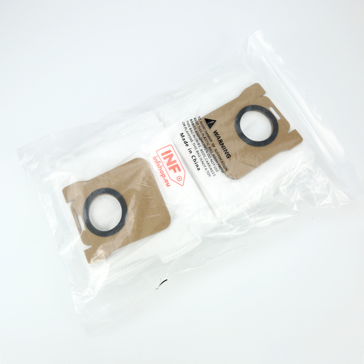 Dwa worki do odkurzacza w przezroczystej plastikowej torbie. Worki są brązowe z czarnymi okręgami, biały materiał filtrujący. Widoczny tekst ostrzegawczy.