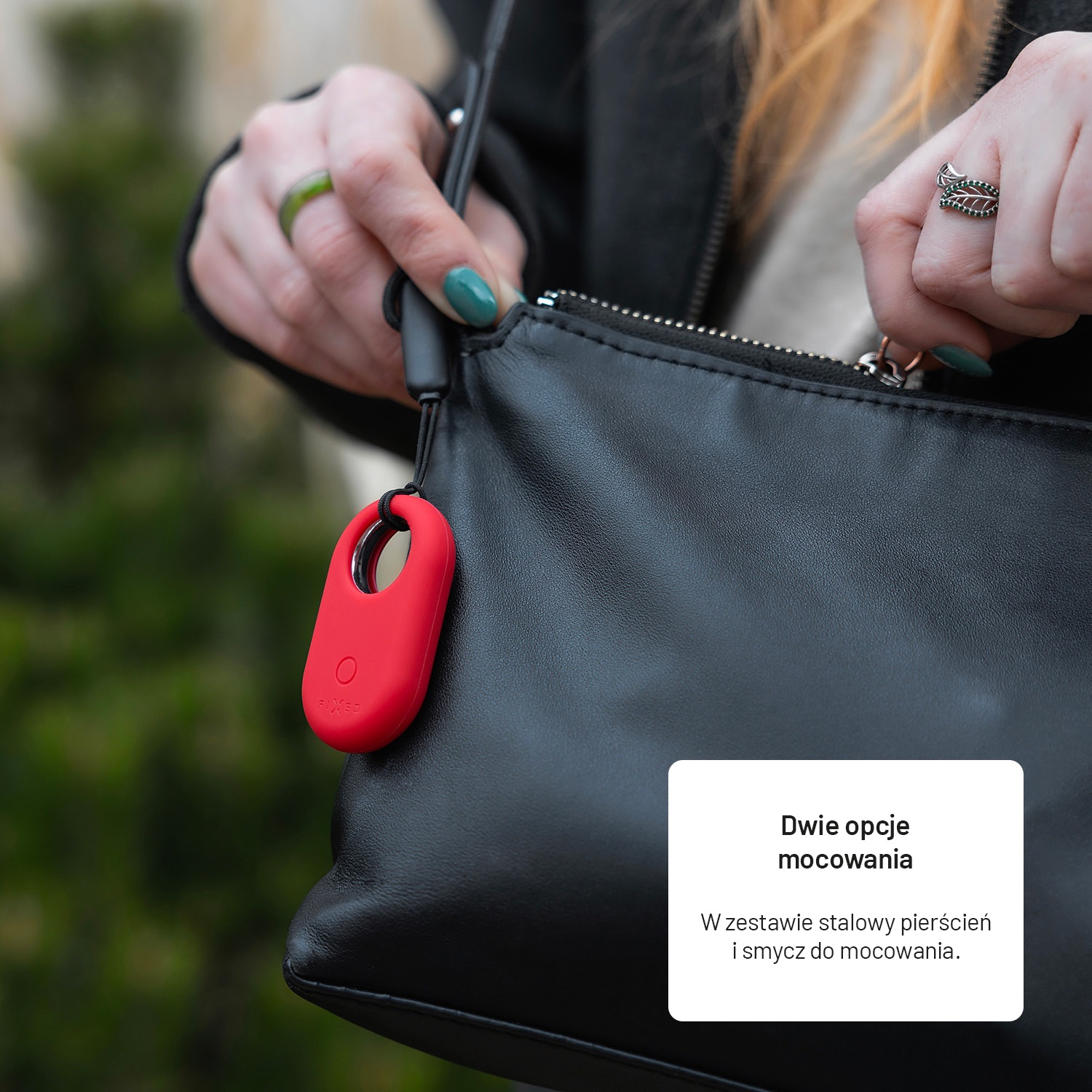 Eine Hand öffnet eine schwarze Handtasche. Ein rotes Etikett hängt daran. Die Frau trägt Ringe und hat grünen Nagellack.