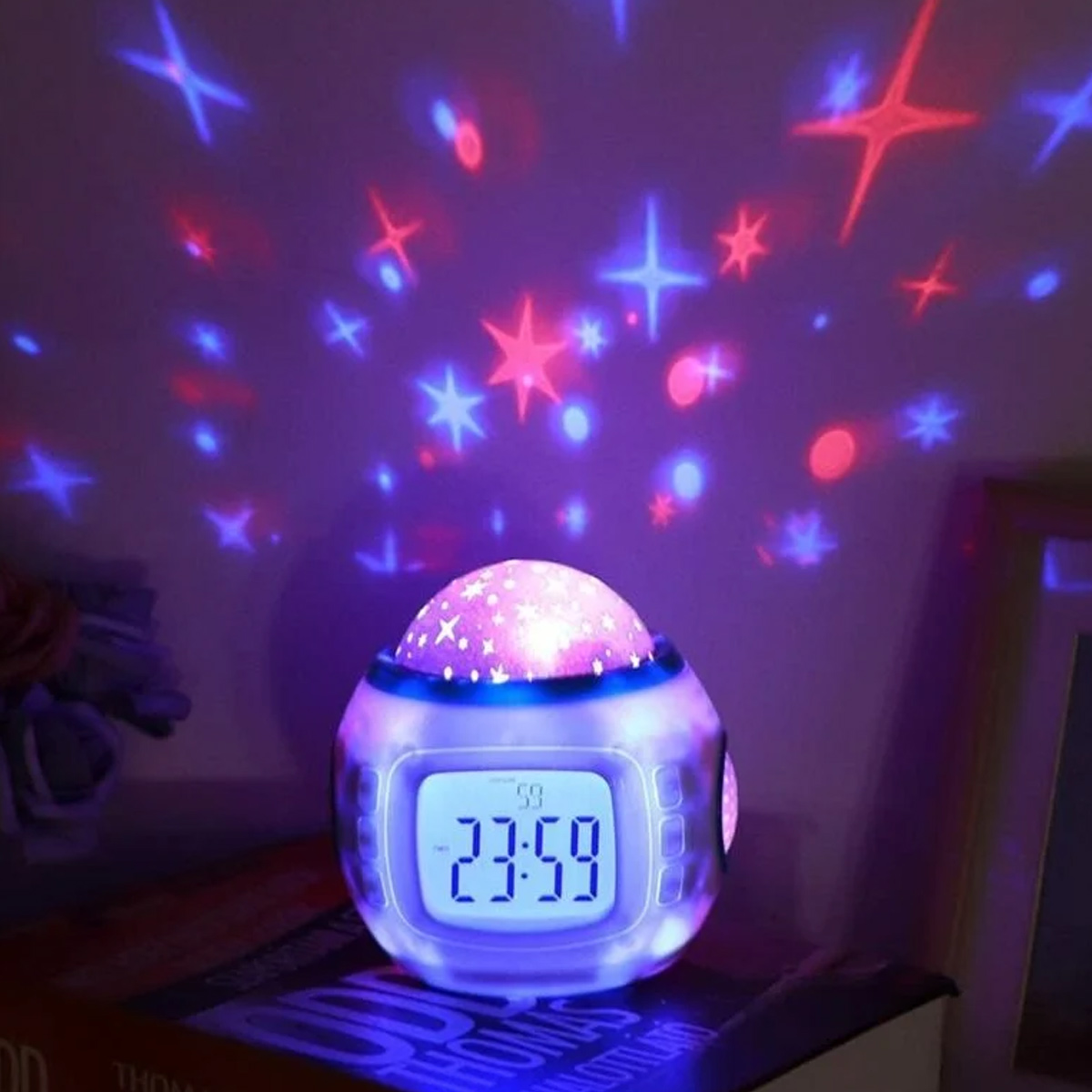 Ein Nachtlicht mit Sternen an der Wand. Es zeigt eine Digitaluhr um 23:59 Uhr. Die Farben sind lila, rot und blau.