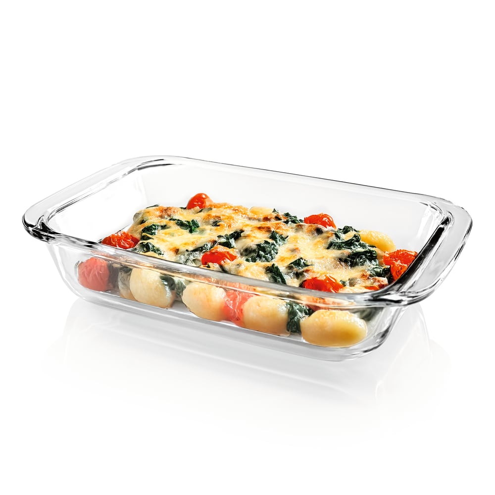 Glasbackform mit gebackenen Gnocchi, Spinat, Kirschtomaten und geschmolzenem Käse auf weißer Oberfläche.