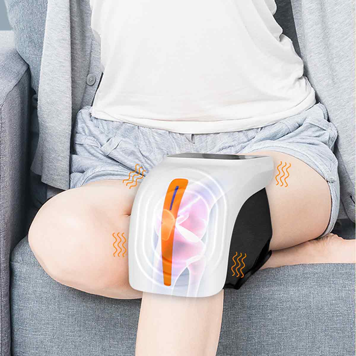 Person in Shorts, sitzt, mit Knie-Therapiegerät. Das Gerät ist weiß mit orangefarbenen und blauen Akzenten, was auf Wärmetherapie hindeutet.