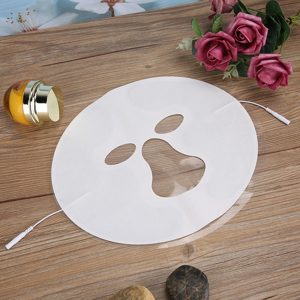 Eine weiße Gesichtsmaske mit Augen- und Mundaussparungen liegt auf einer Holzoberfläche. Rosen und eine Flasche sind ebenfalls vorhanden.