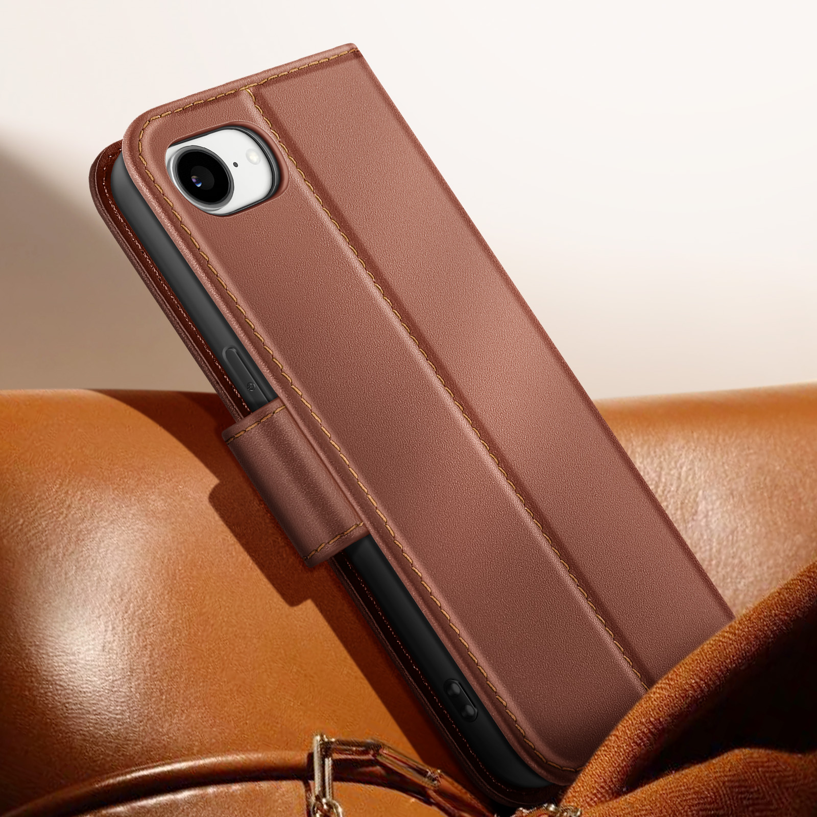 Una custodia per telefono in pelle marrone con bordi cuciti, appoggiata su una superficie in pelle marrone, con una catena dorata.