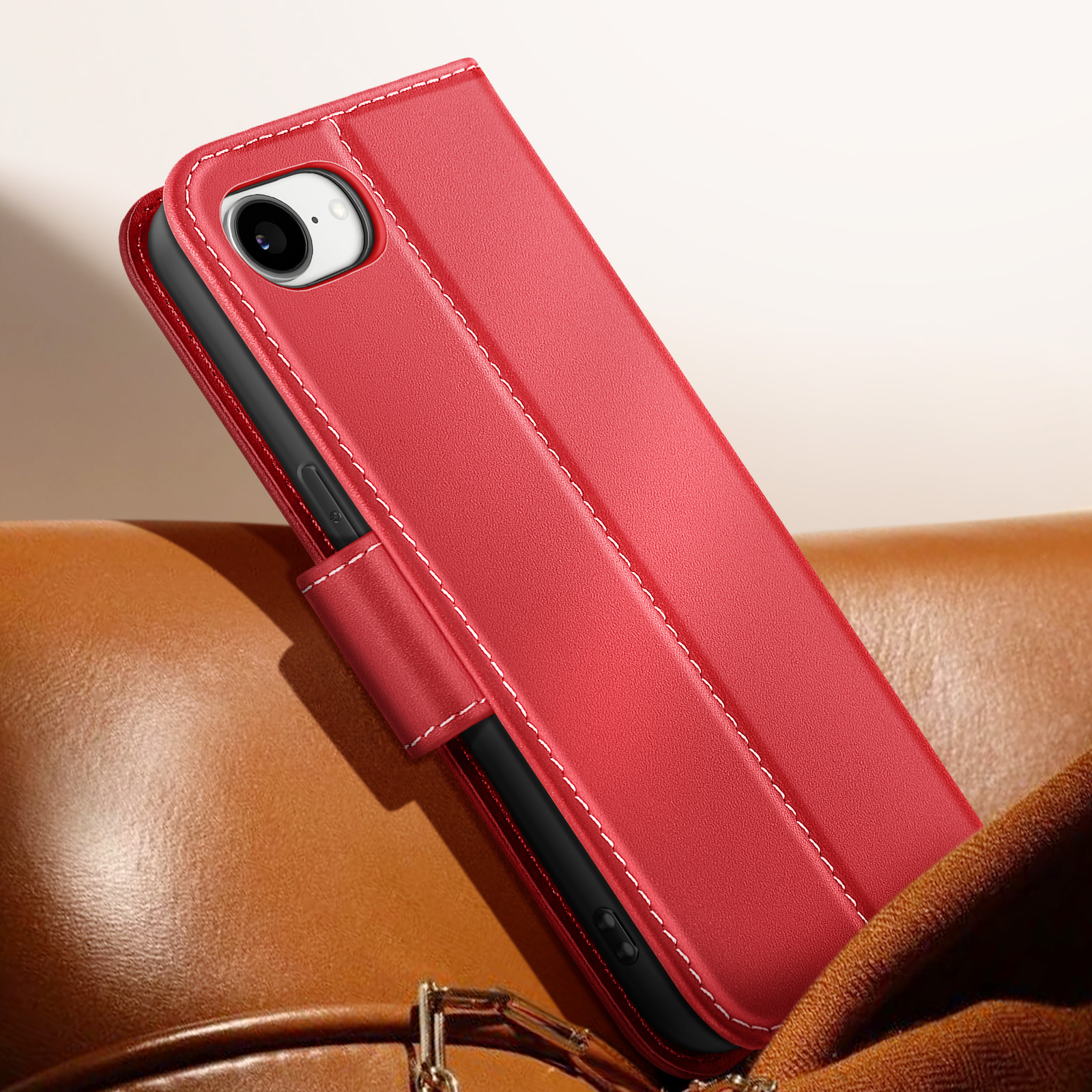 Una custodia per telefono in pelle rossa con cuciture bianche è aperta, rivelando un telefono. Poggia su una superficie in pelle marrone.