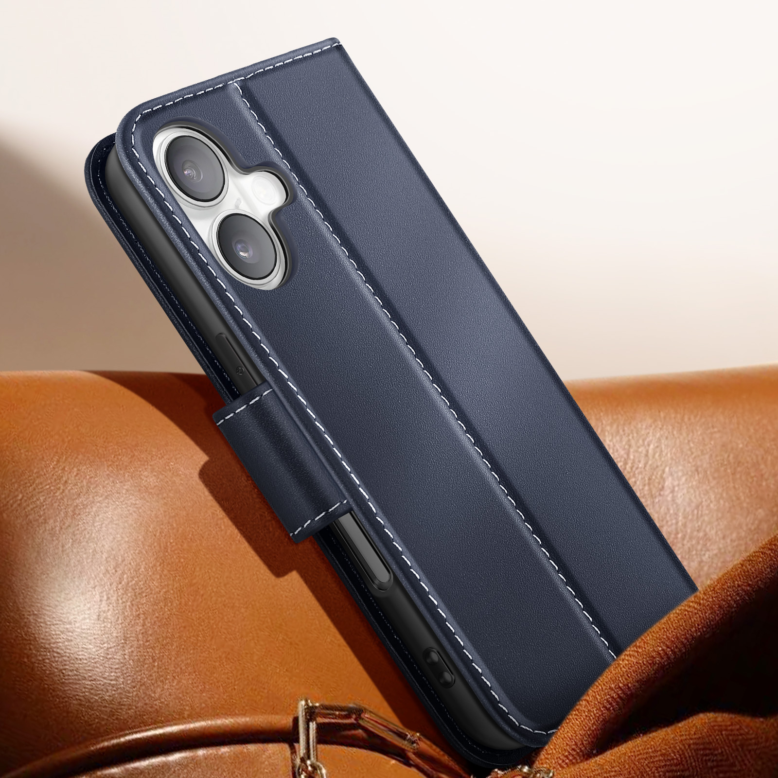 Una custodia per telefono blu scuro con cuciture bianche. Poggia su una superficie in pelle marrone, coprendo parzialmente un telefono.