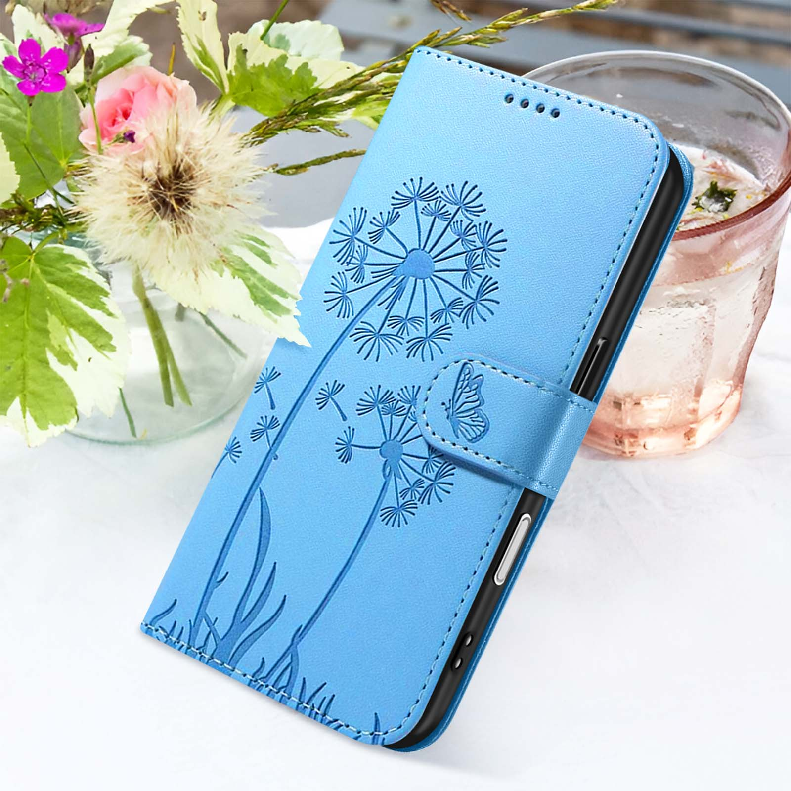 Custodia blu per telefono con design di dente di leone, chiusura a farfalla. Fiori e un bicchiere d'acqua sullo sfondo.