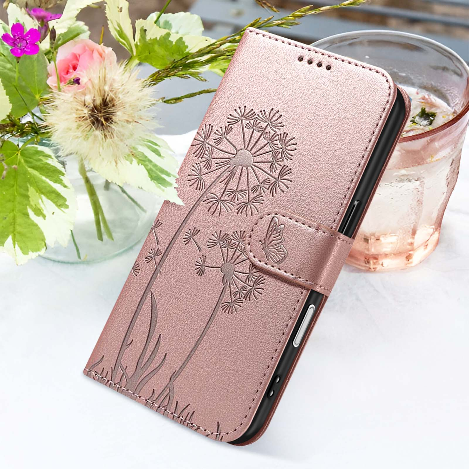 Eine roségoldene Handyhülle mit Pusteblumen-Design, neben Blumen und einem Glas Wasser.