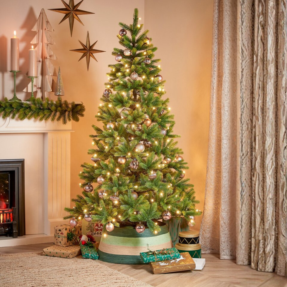 A decorated Christmas tree with lights and ornaments stands near gifts. A fireplace and curtains are in the background.