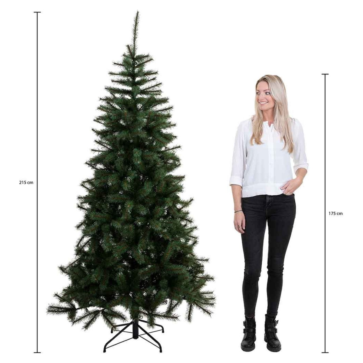 Un grand sapin de Noël vert se tient à côté d'une femme portant une chemise blanche et un pantalon noir. L'arbre mesure 215 cm.