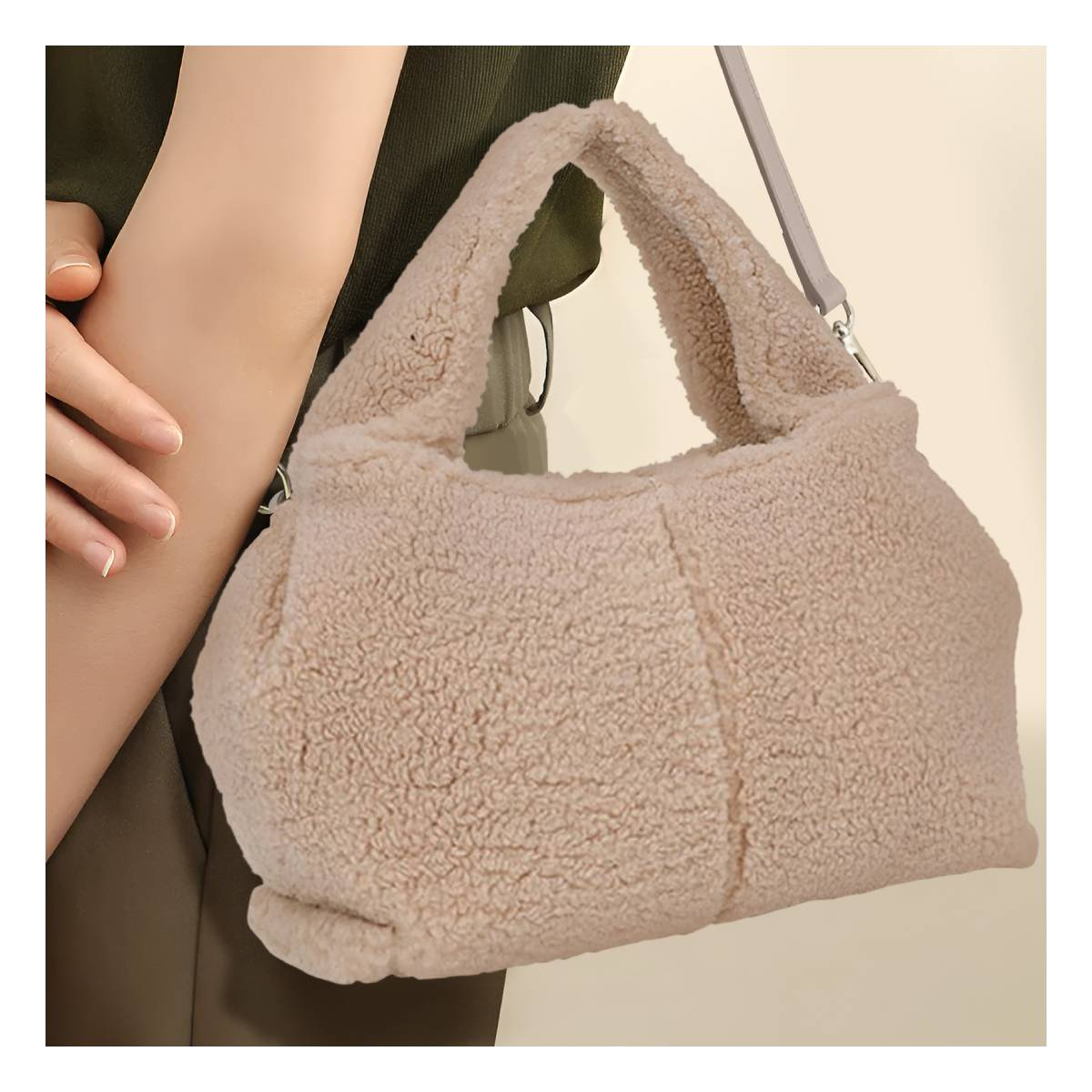 Una bolsa beige y esponjosa con correa es sostenida por una persona. La textura de la bolsa es suave y el fondo es neutro.