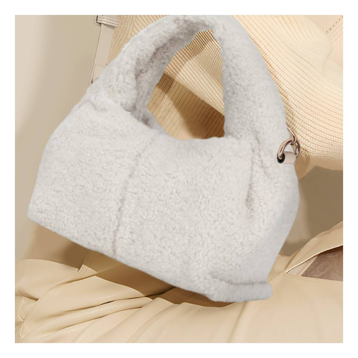 Eine flauschige, weiße Handtasche mit Griff. Im Hintergrund ein beiger Pullover und eine Lederjacke. Ein Metallring ist sichtbar.