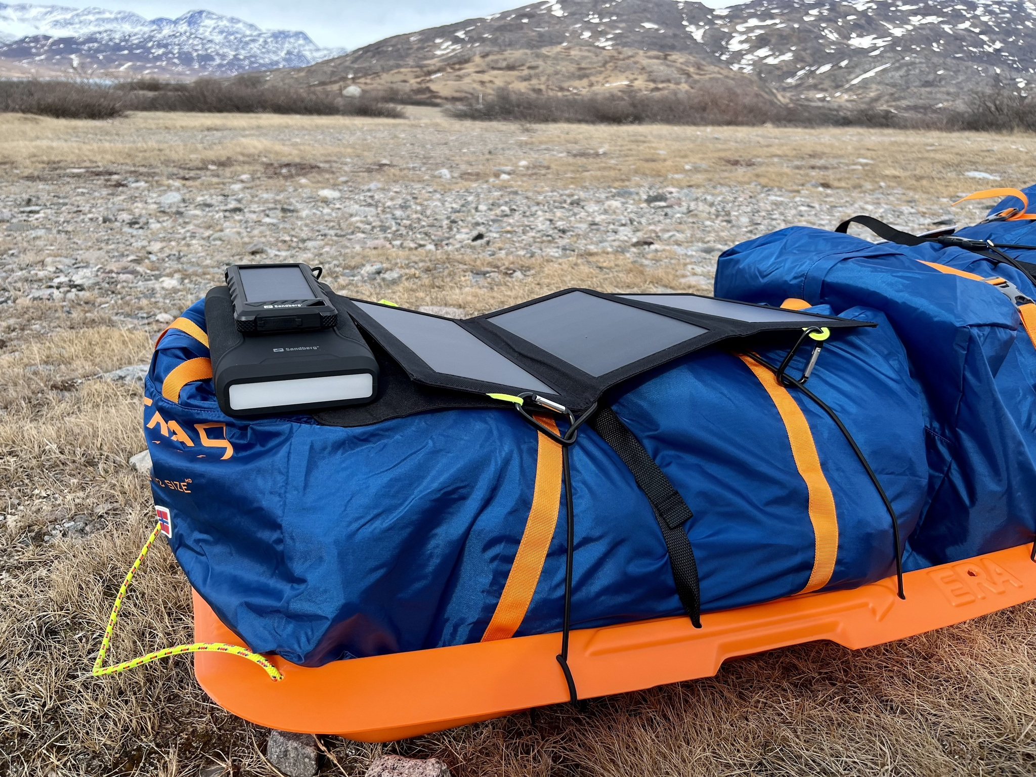 Blaue Tasche auf orangefarbenem Schlitten mit Solarpanel und Gerät, Berge im Hintergrund.