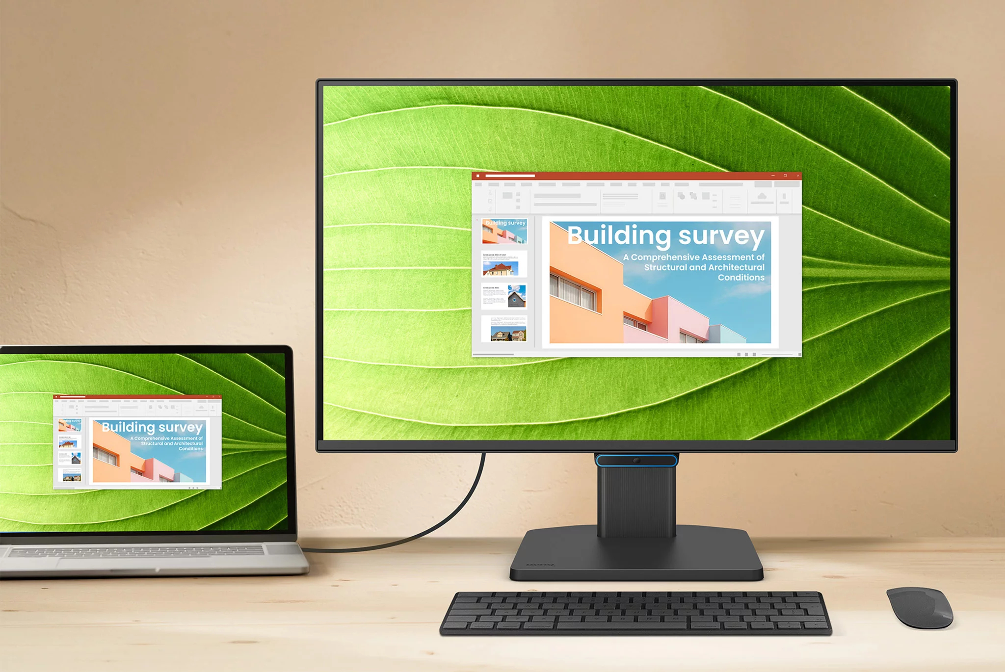 Een laptop en een monitor tonen een presentatie met de titel 'Building Survey'. Een toetsenbord en muis liggen op het houten bureau.