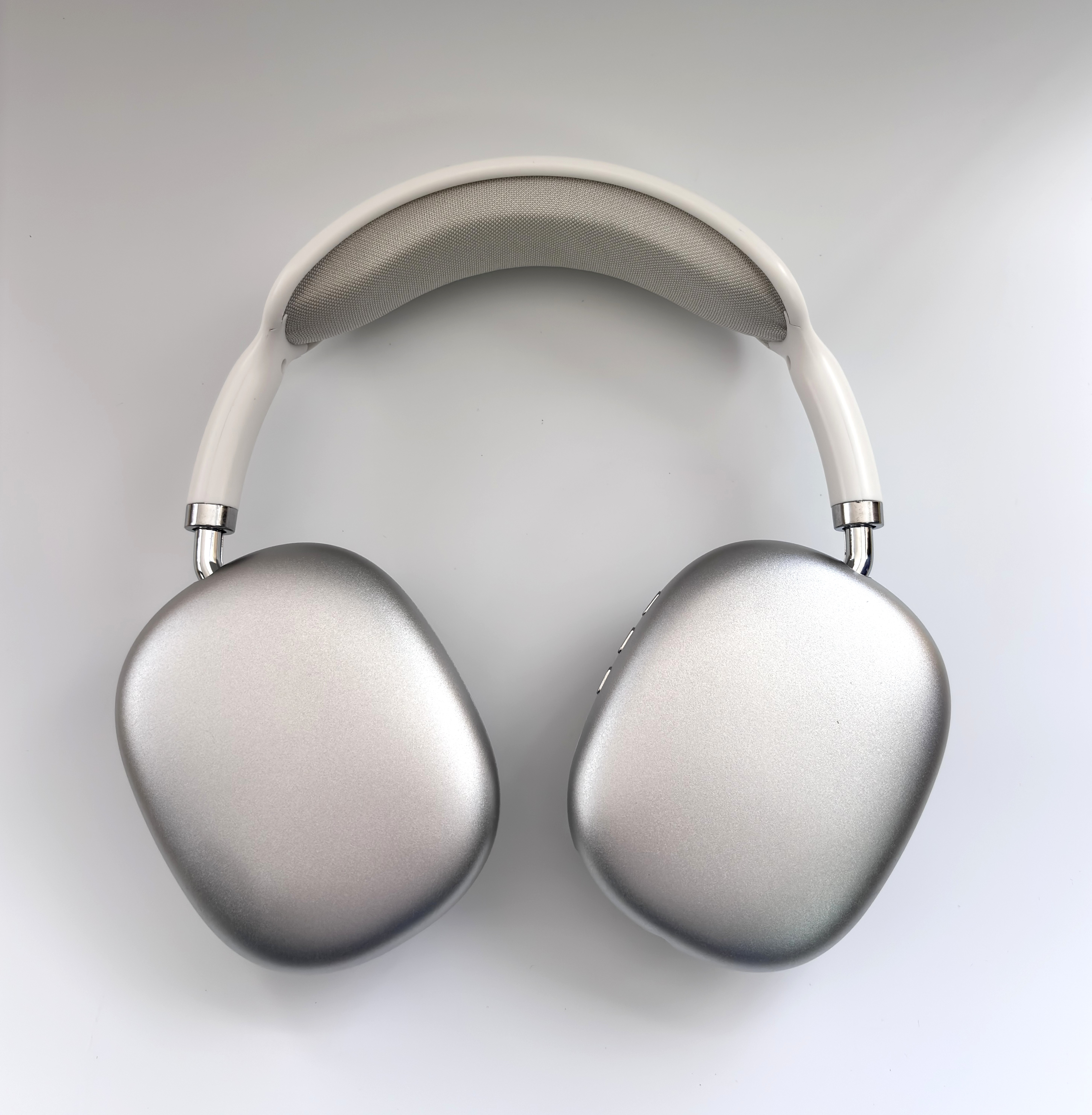 Toma cenital de auriculares Apple plateados. La diadema es blanca con malla gris. Las orejeras son plateadas sobre fondo blanco.