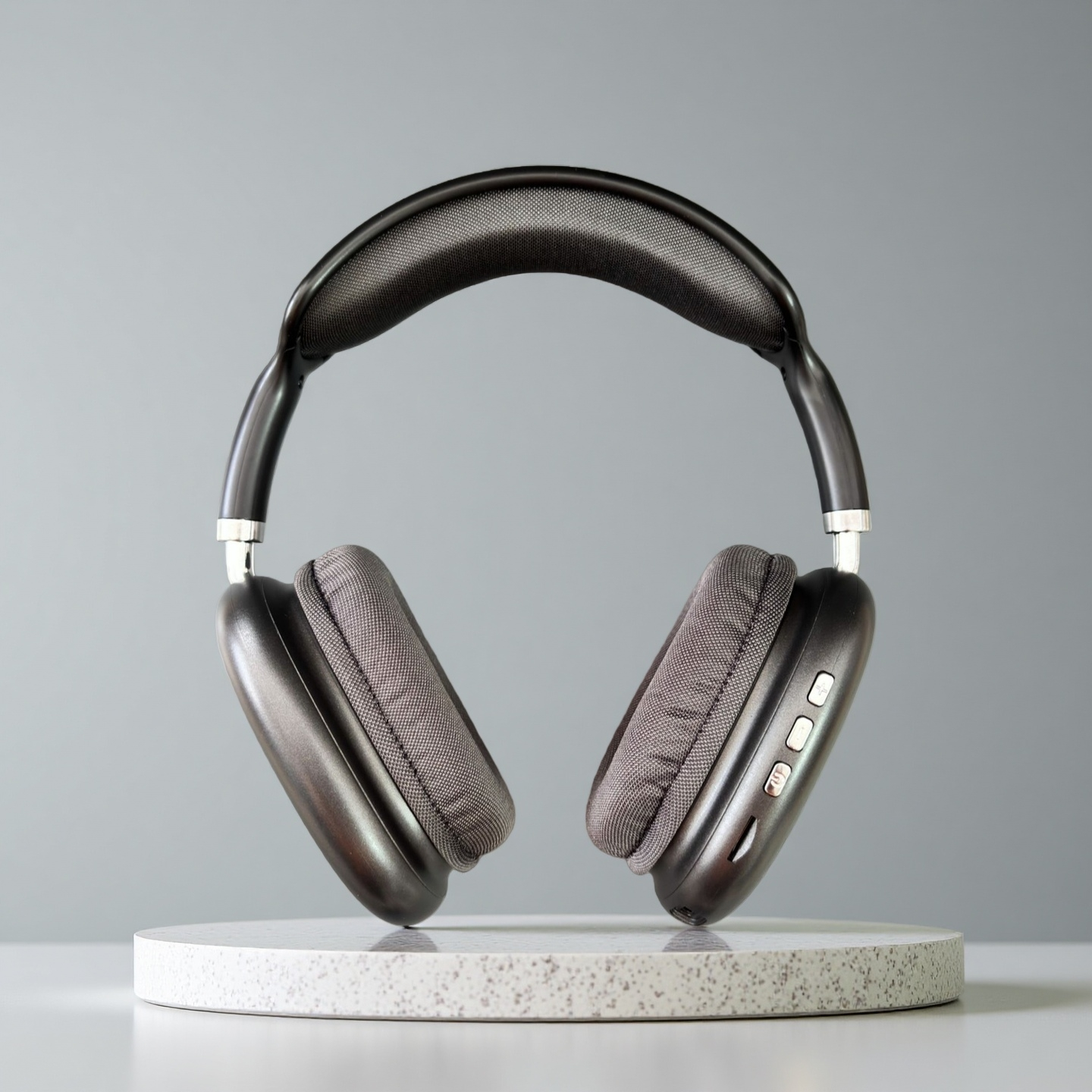 Auriculares negros con almohadillas grises sobre una plataforma blanca moteada contra un fondo gris.