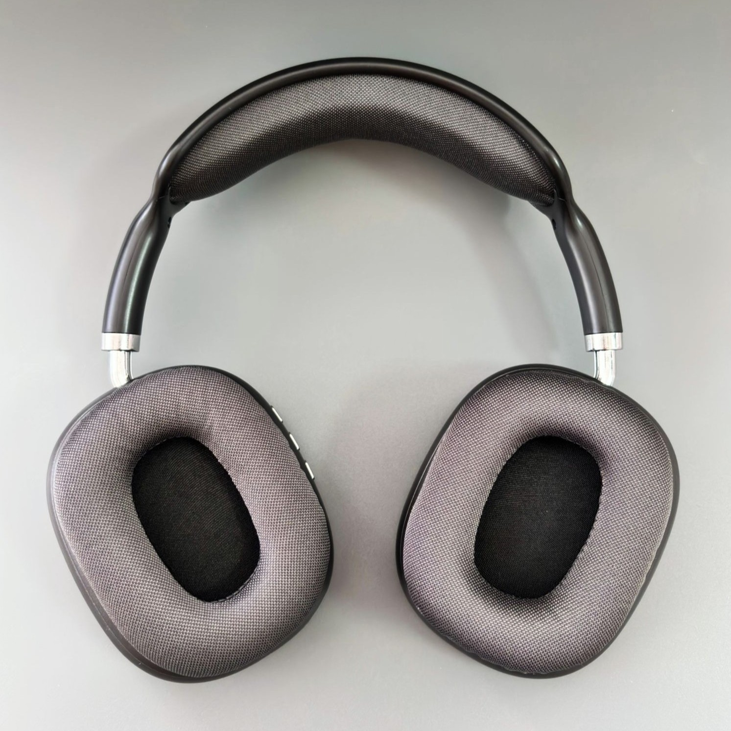 Auriculares supraaurales sobre una superficie gris. Marco negro, almohadillas grises y diadema acolchada. Acentos plateados.