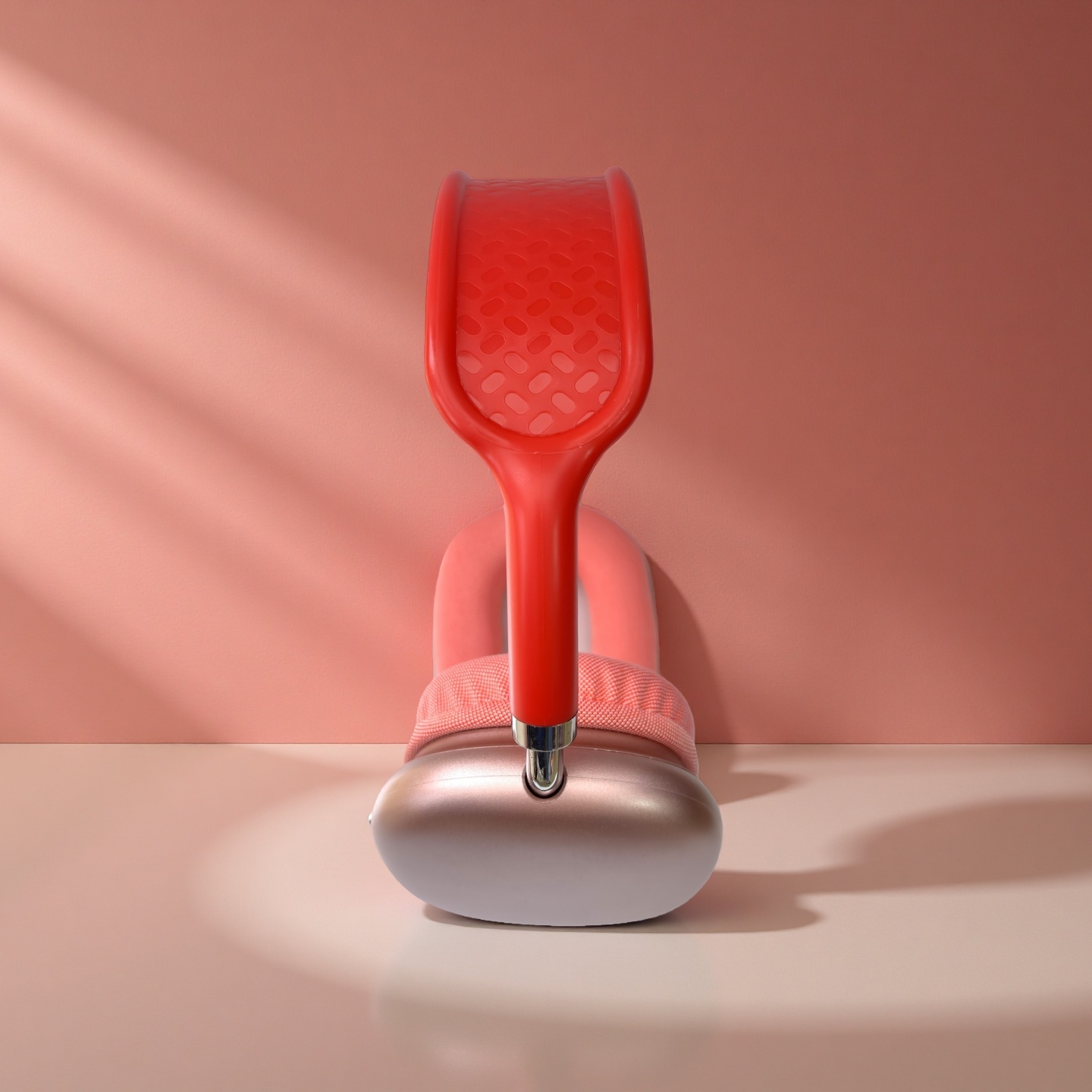 Auriculares rojos y plateados sobre una superficie clara contra una pared rosa. Los auriculares están centrados, con luz y sombra.
