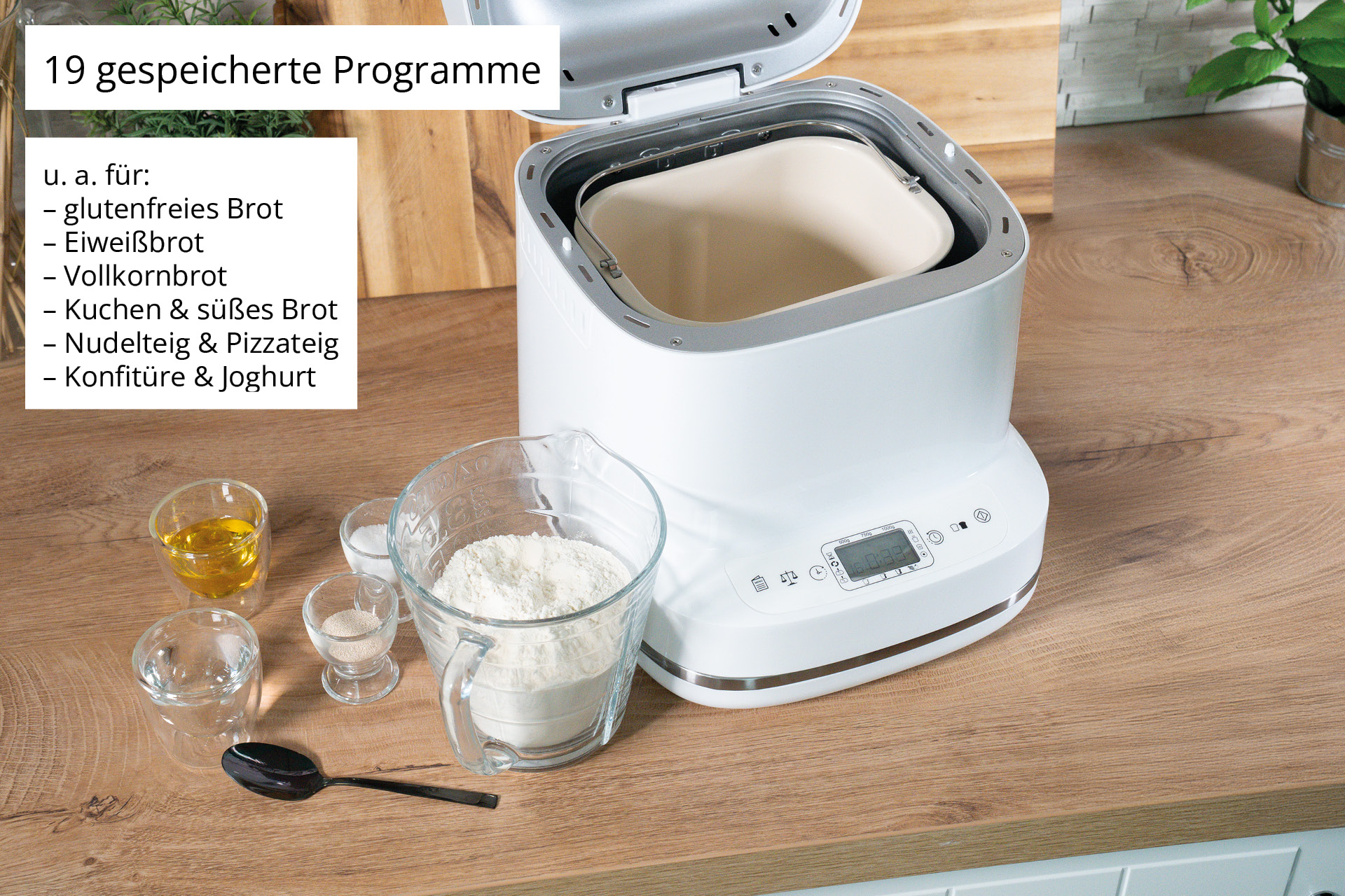 Weißer Brotbackautomat mit Zutaten wie Mehl, Öl und Wasser auf Holzoberfläche.