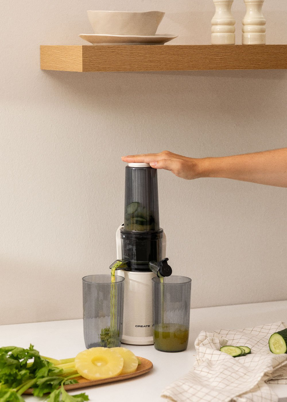 Una exprimidora extrae jugo de pepinos. Se llenan dos vasos. Se ven piña, apio y un pepino.