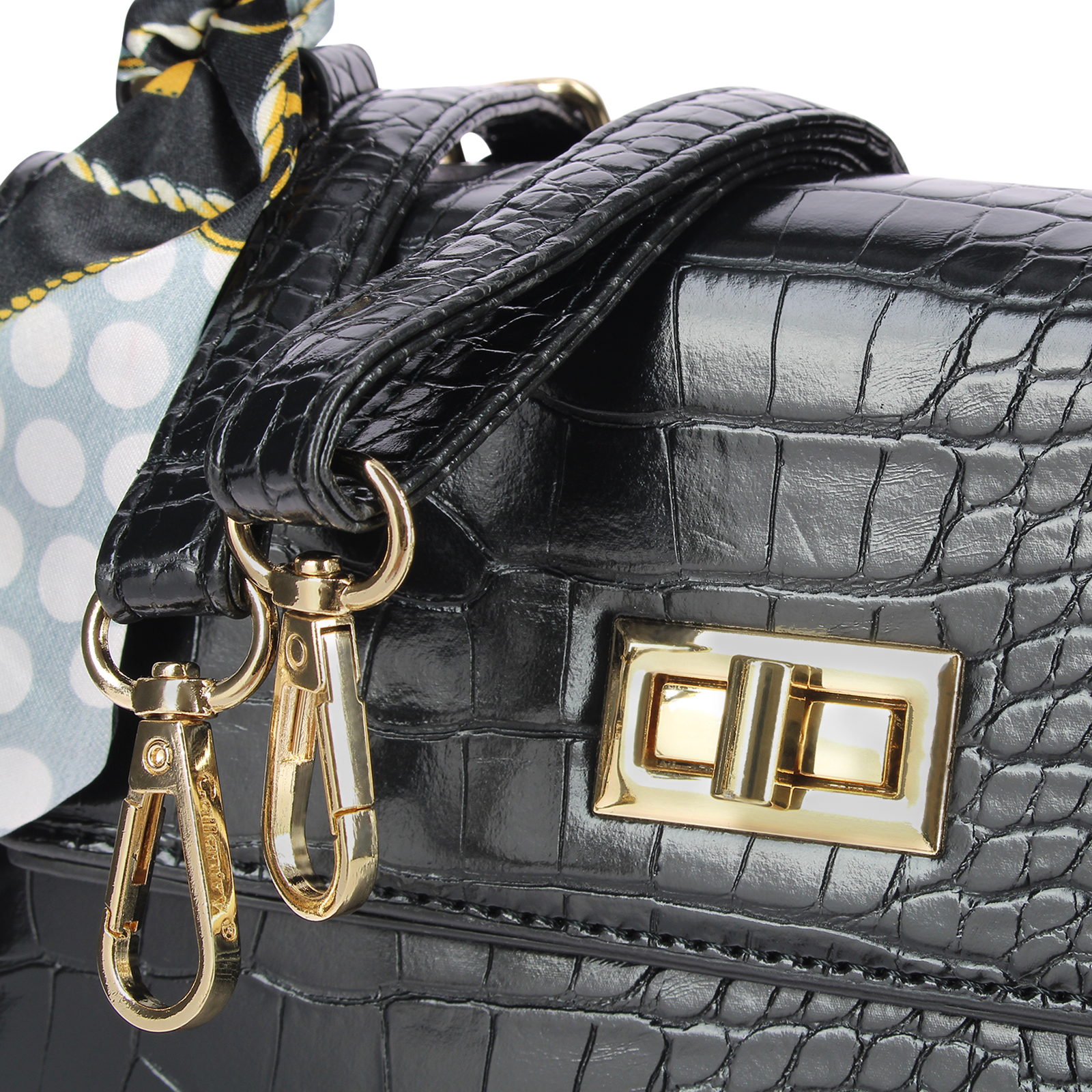 Bolso de cuero negro con cierres dorados y pañuelo estampado. El bolso tiene una superficie texturizada y un cierre dorado.