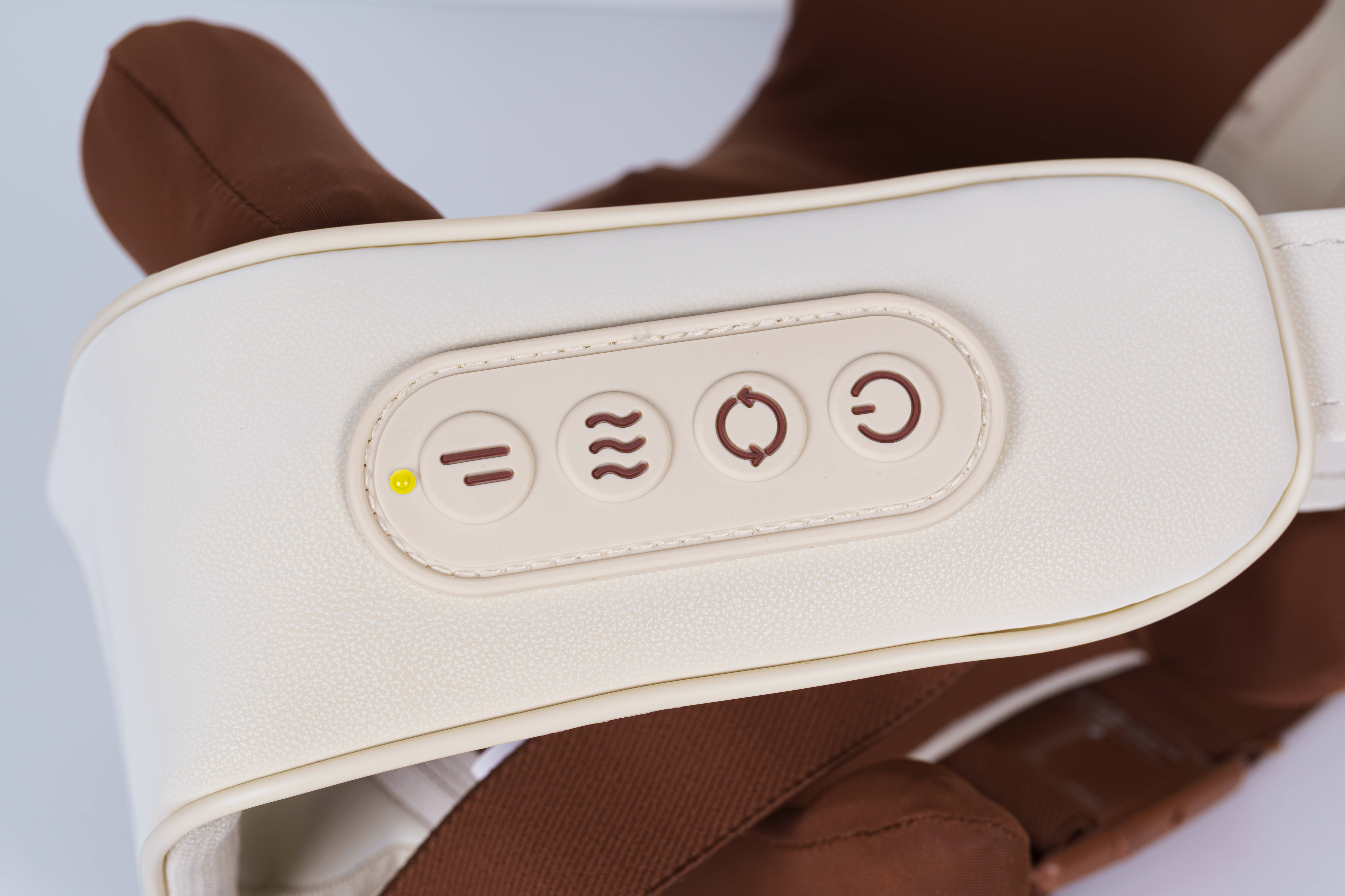 Kremowe urządzenie do masażu z przyciskami sterowania. Brązowa tkanina widoczna w tle.